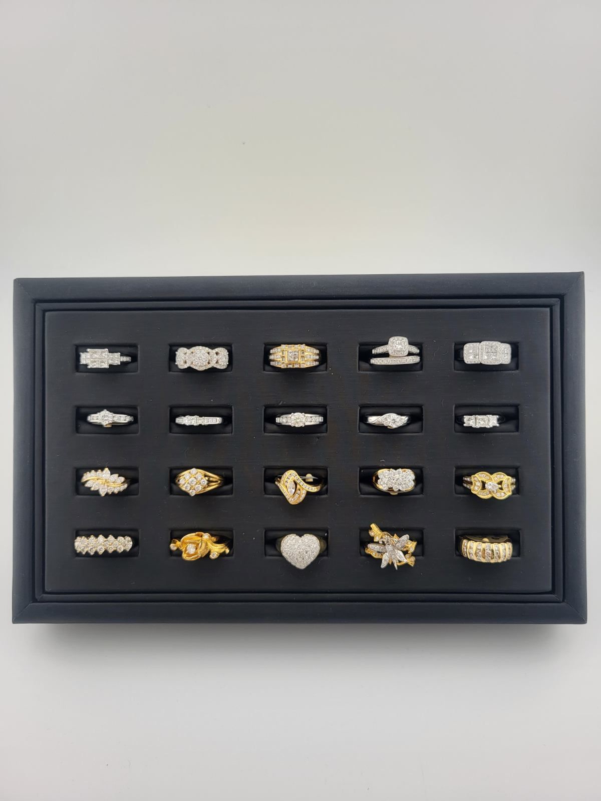 Framed display of assorted decorative rings in multiple rows on a light background