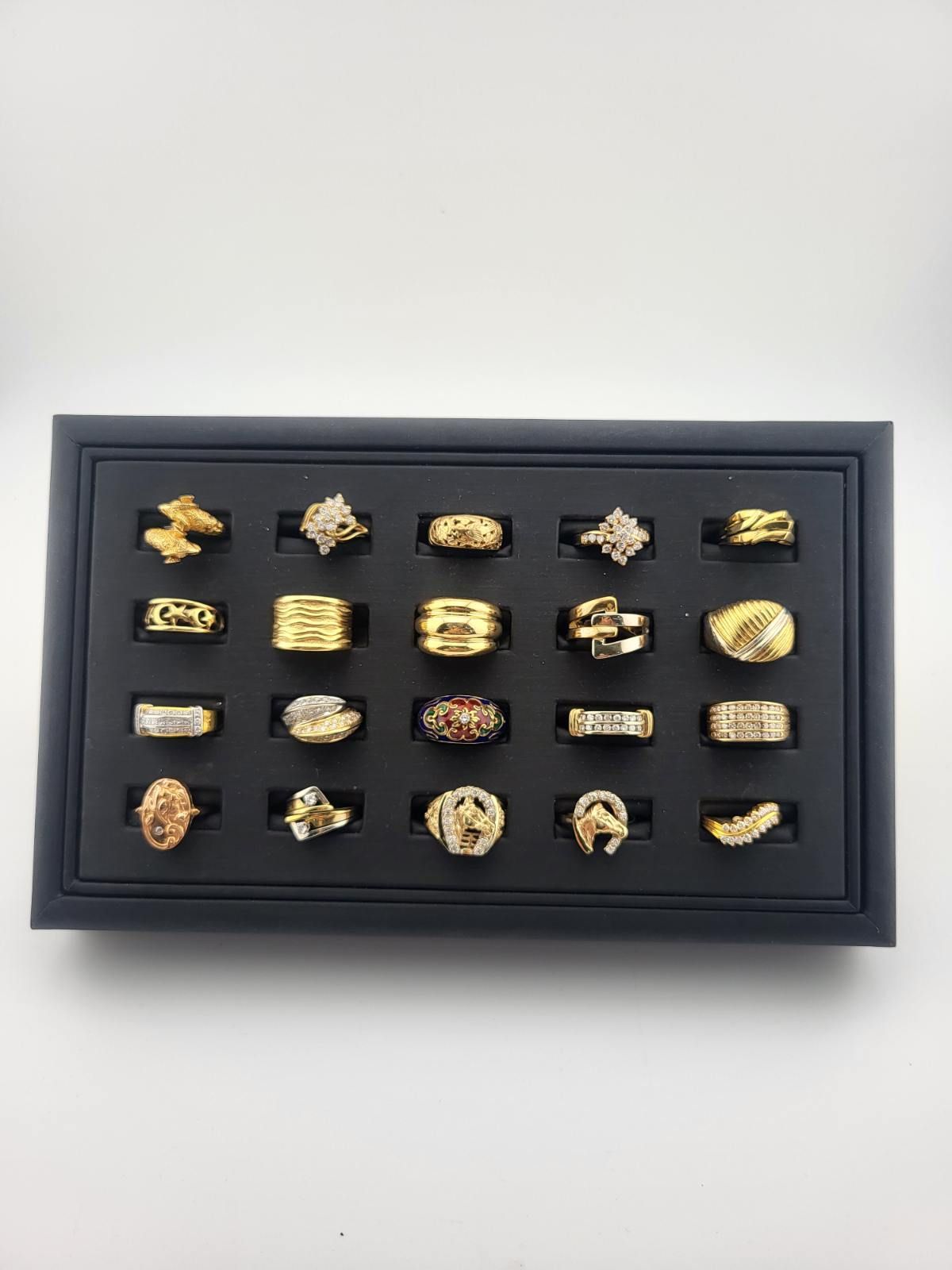 Framed display of assorted gold and silver rings arranged on a black background.