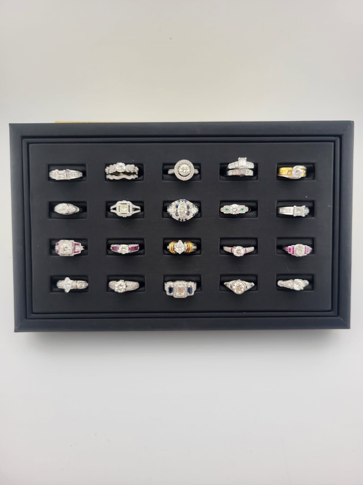 Framed display of 15 rings arranged in a grid on a light wall.
