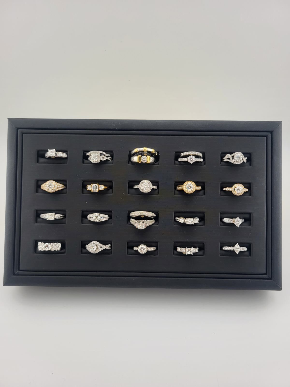Framed display of 20 small assorted rings on a dark background