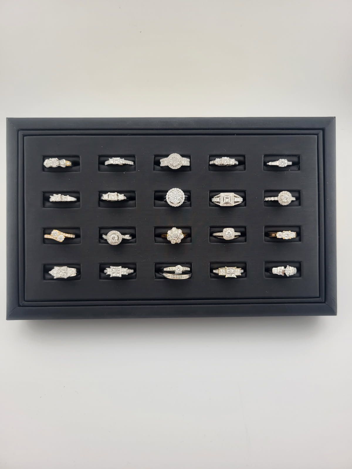 Dark gray display case with 16 small white sample stones in a grid on a white wall
