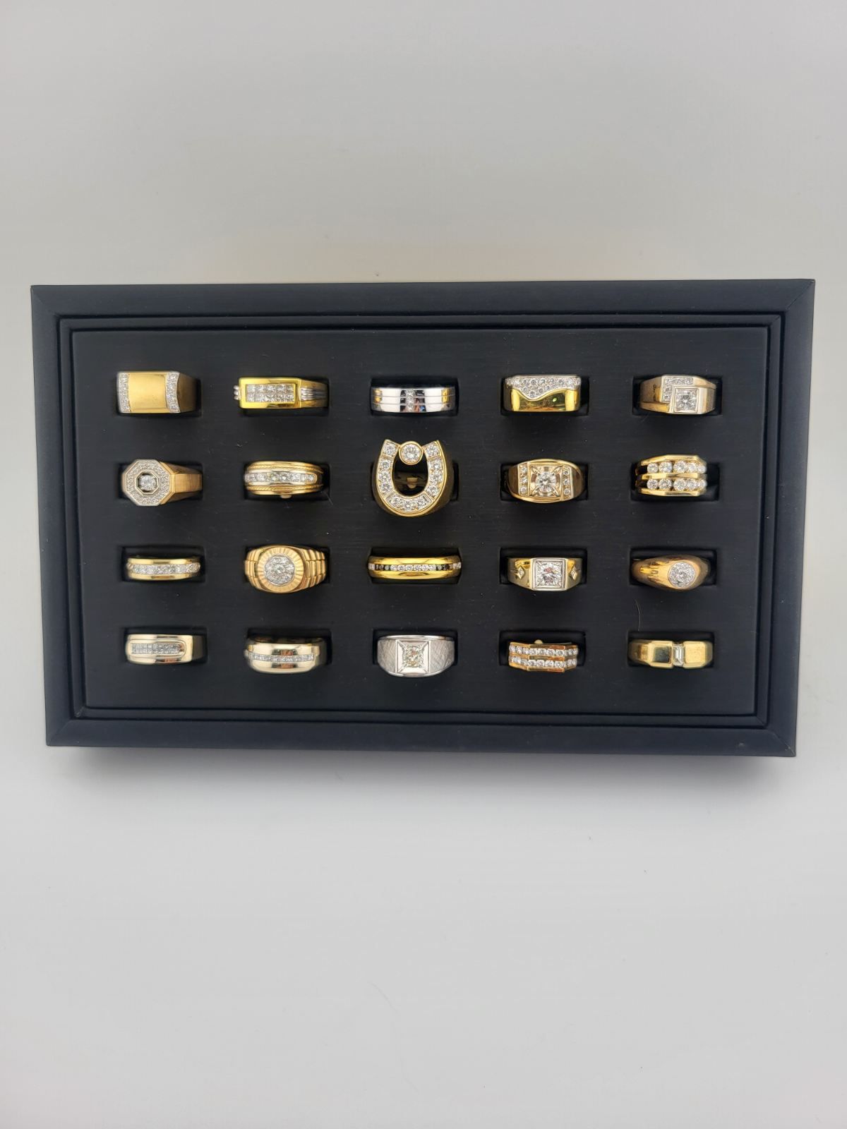 Black display case with rows of gold and silver rings on a dark background