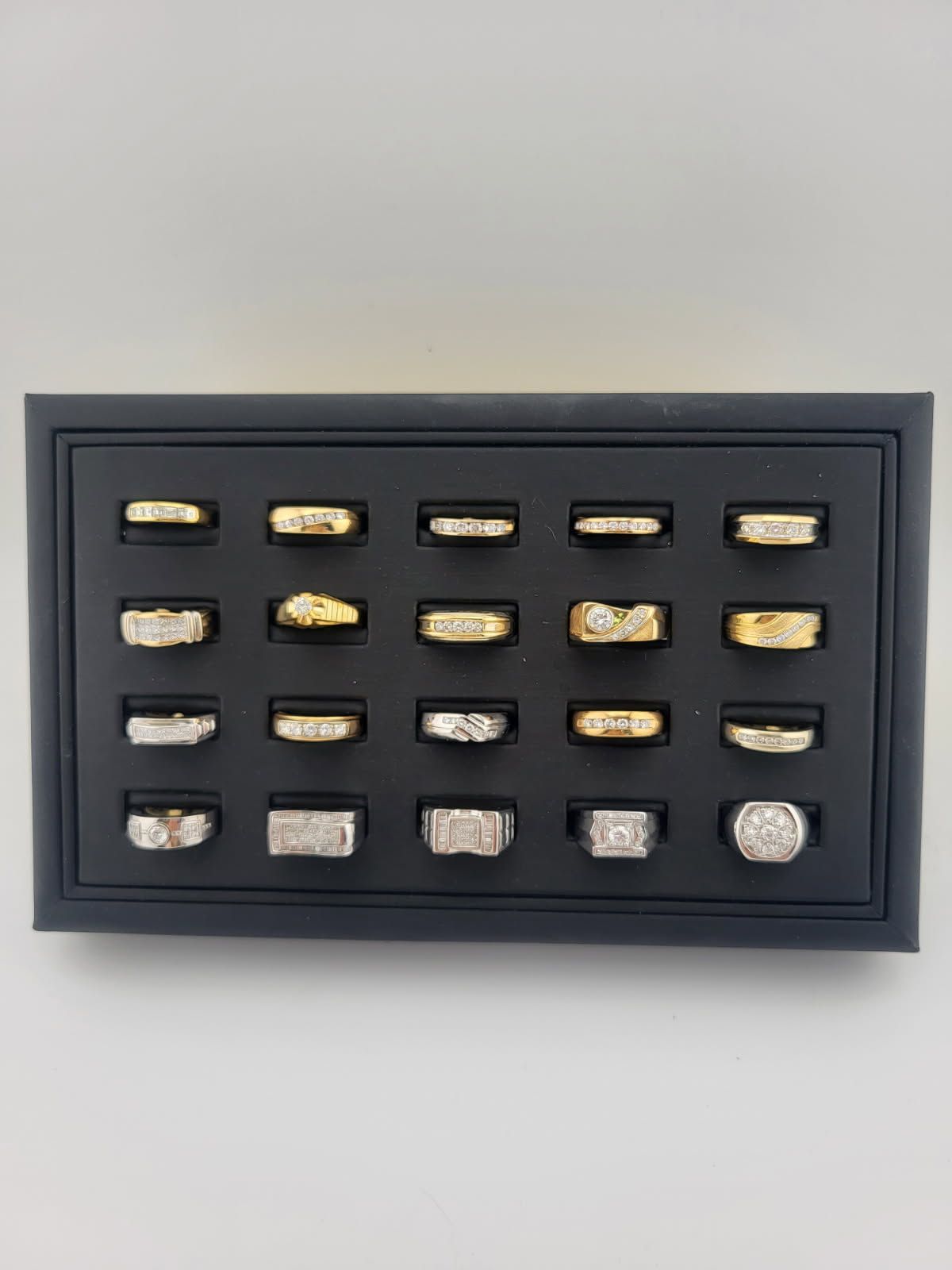 Black display case with rows of small gold and silver metal pieces against a light wall