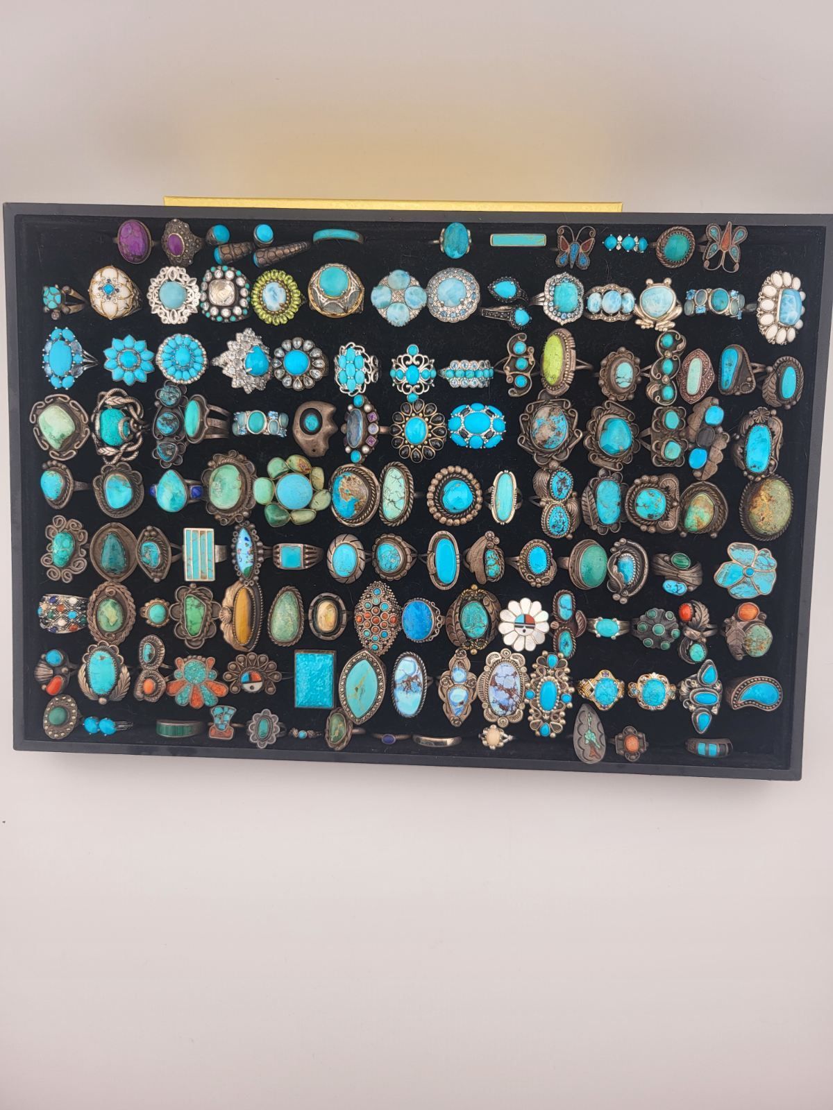 Framed display of many colorful turquoise and blue jewelry pieces on a black background