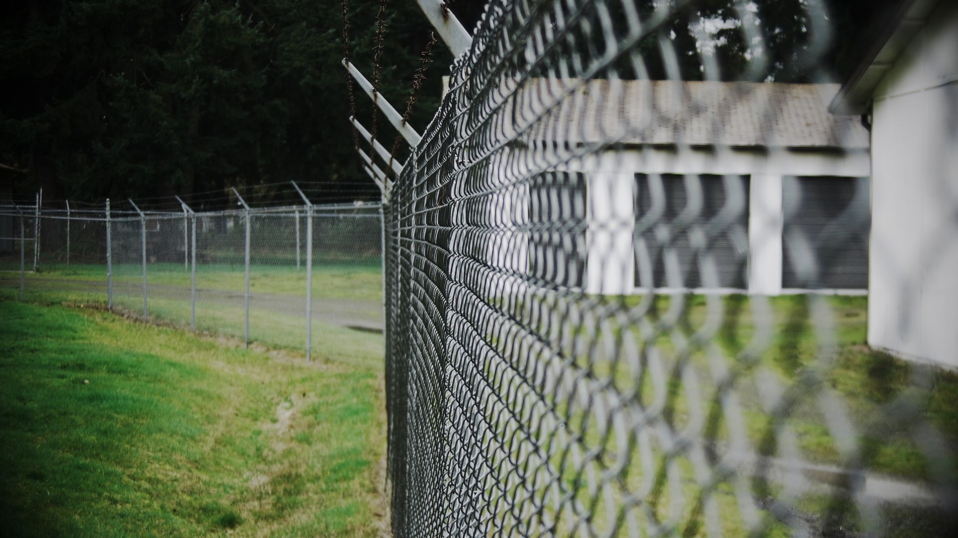 Chain-link security fence topped with barbed wire near a building.