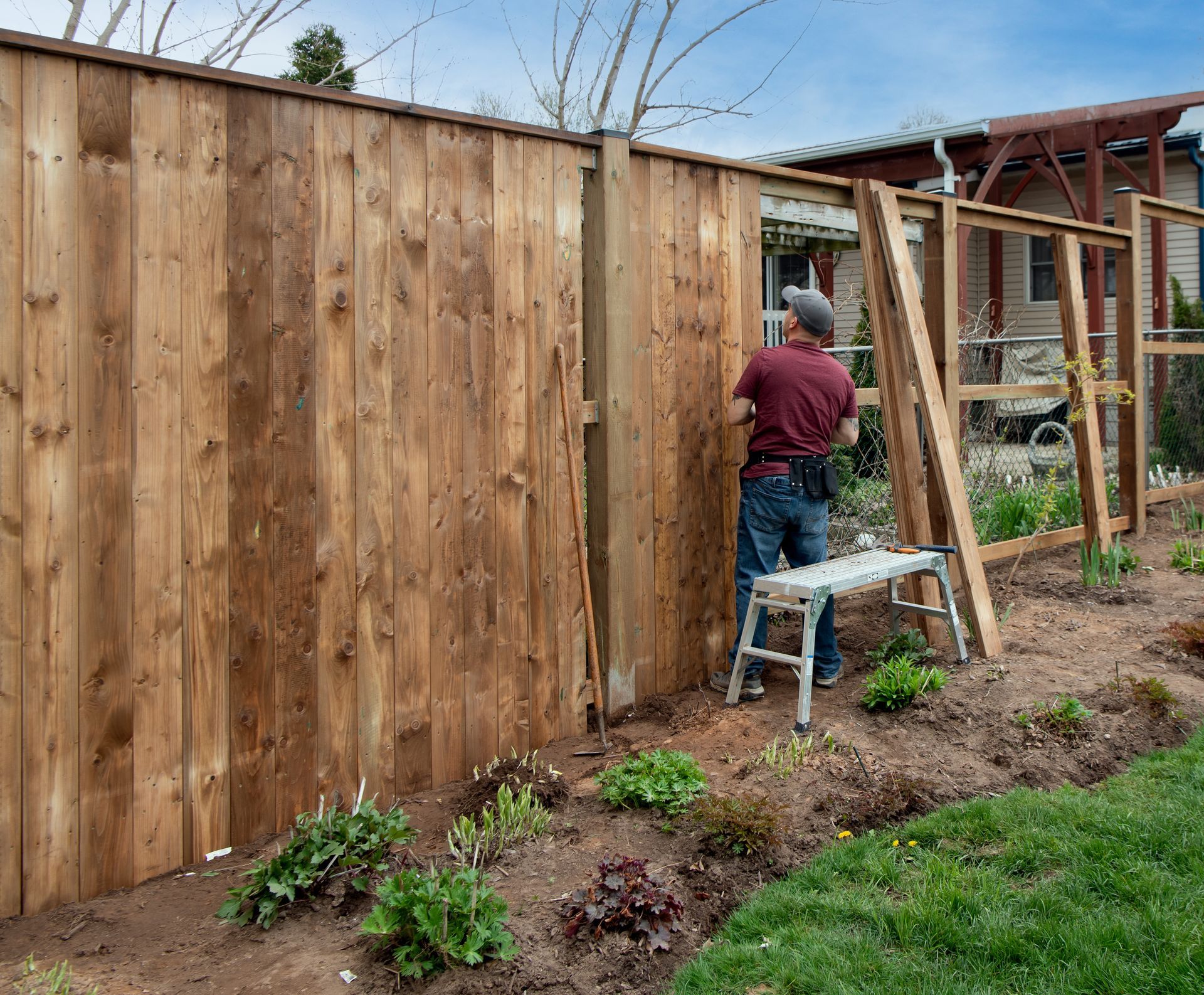 Worker installing a tall wooden privacy fence in a backyard garden.