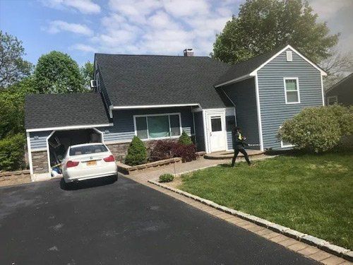A white car is parked in front of a blue house.