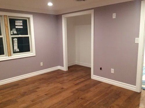 An empty room with purple walls and hardwood floors.