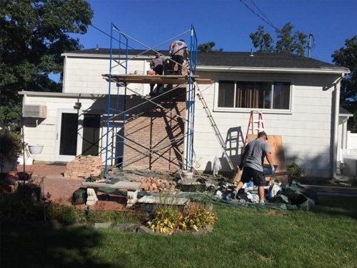 A man is standing on a scaffolding in front of a house.
