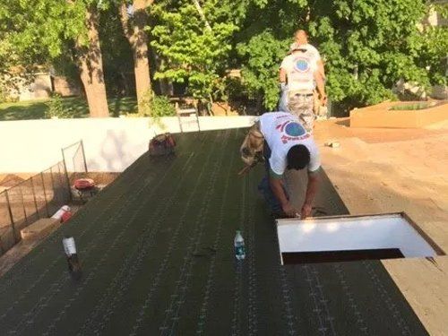 A group of men are working on a roof and one of them is wearing a shirt that says ' a ' on it