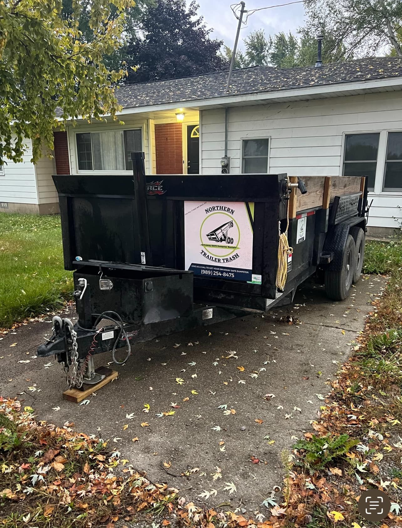 Black dump trailer parked on a concrete driveway in front of a house.