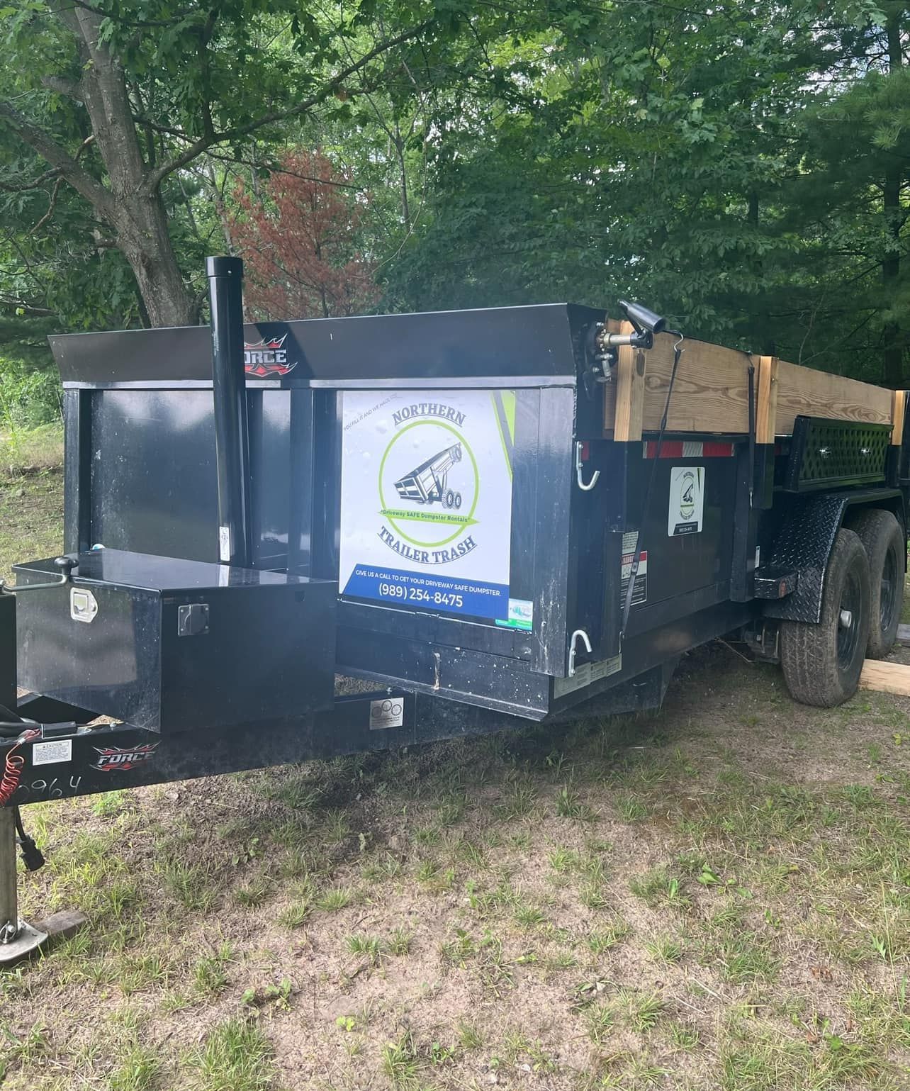 Black dump trailer parked on grass, with business logo on the side.