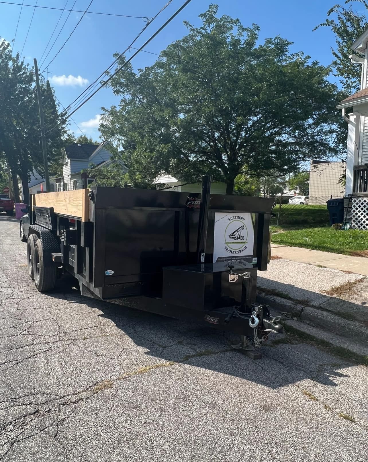 Black trailer parked on a cracked street; it has a wooden bed and a sign on the front.