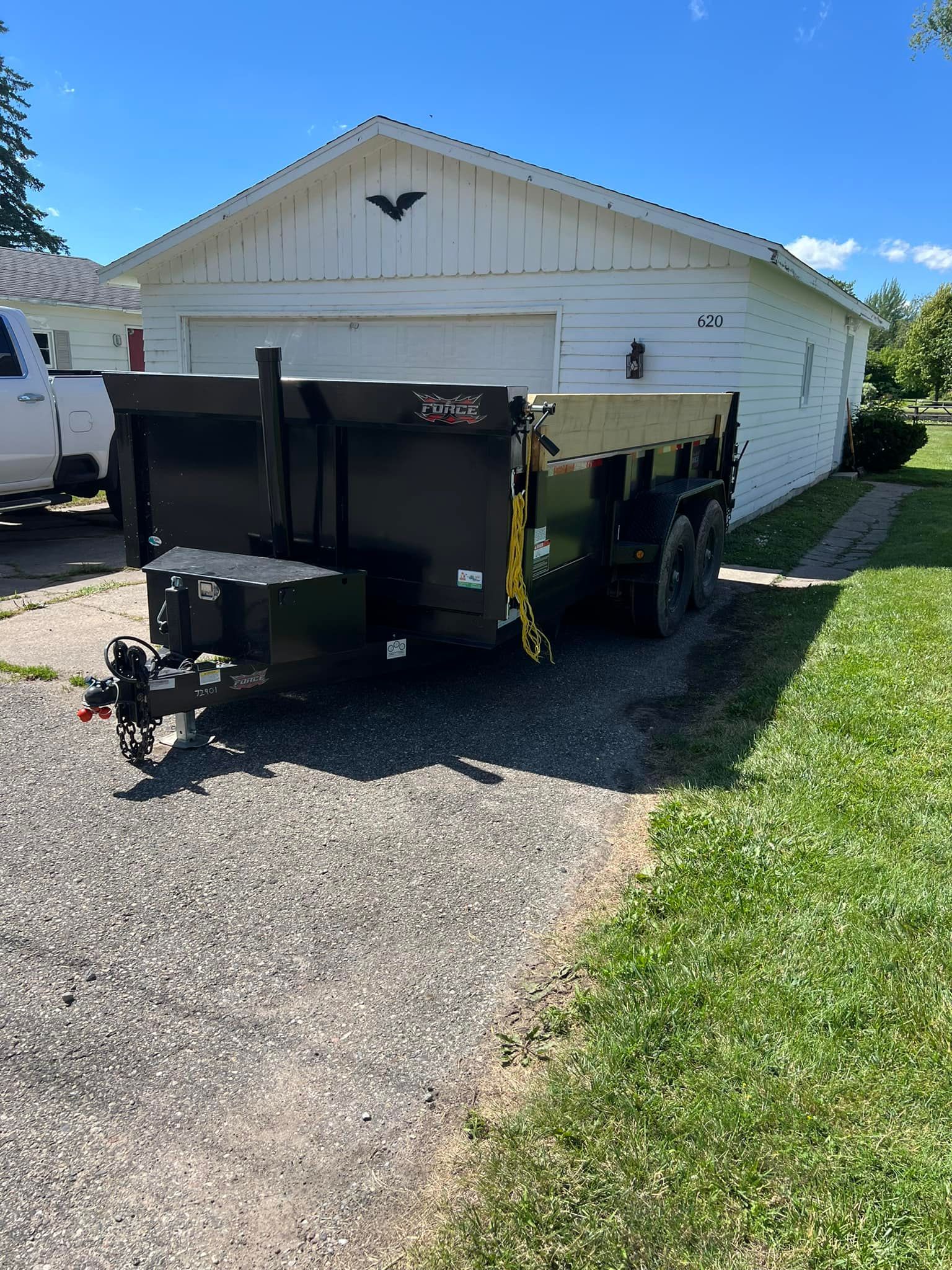 Black dump trailer on a driveway in front of a white garage on a sunny day.