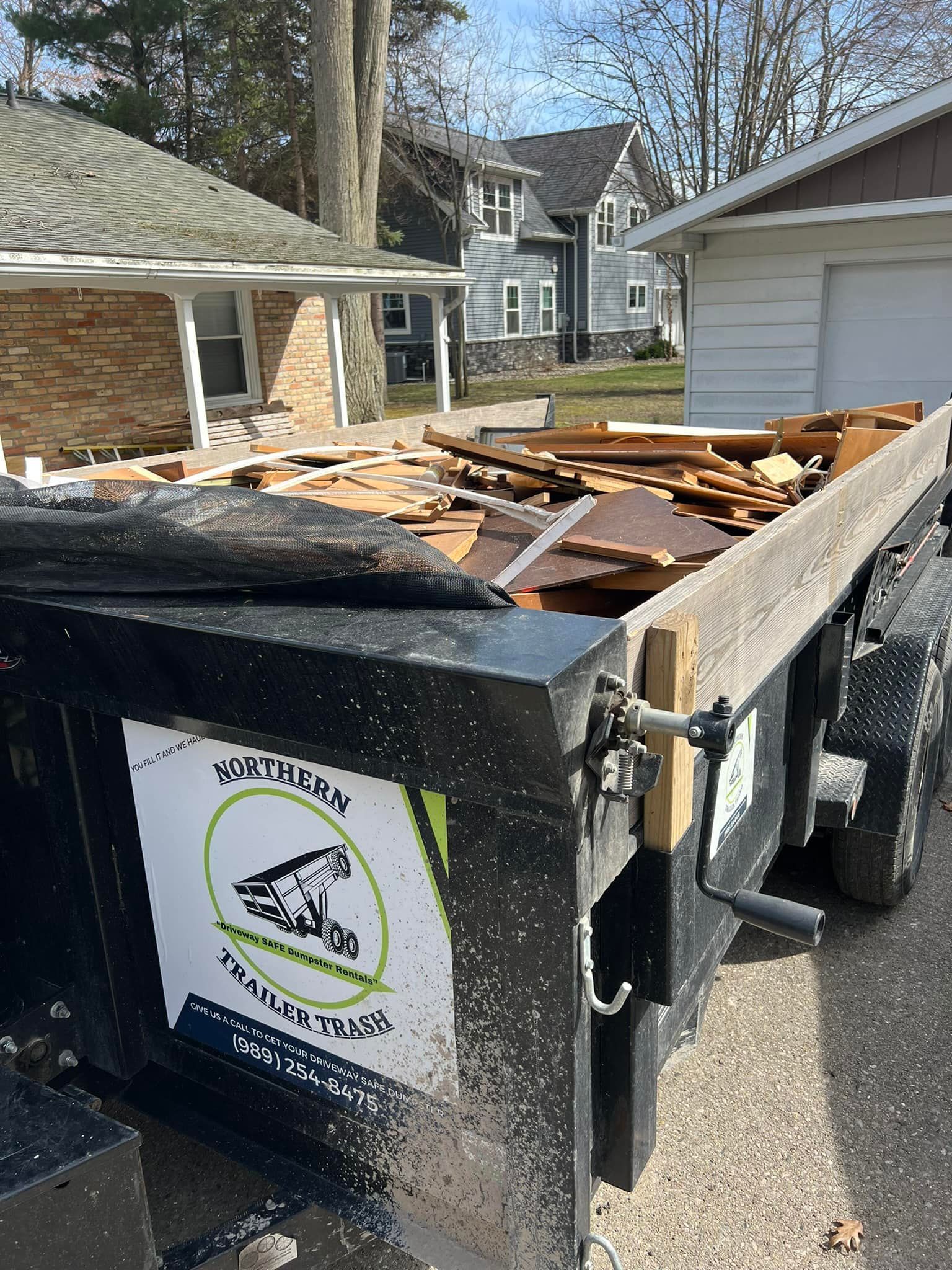 Black trailer filled with wood debris; logo says 