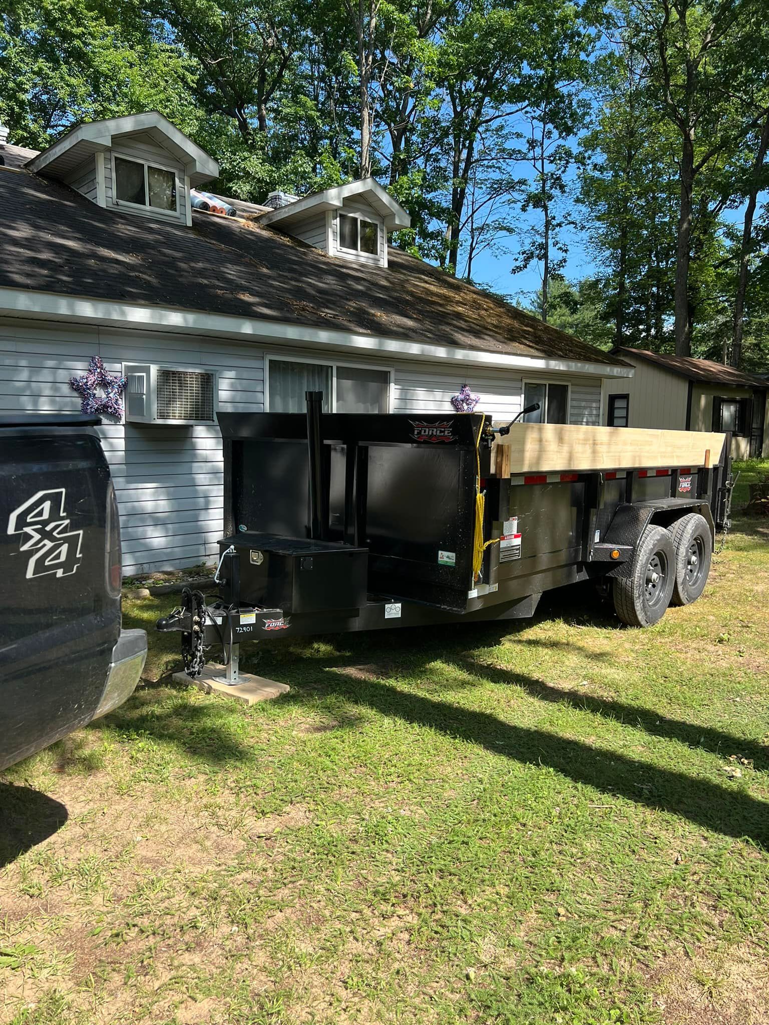 Black trailer hitched to a truck parked in front of a house on a grassy lawn.