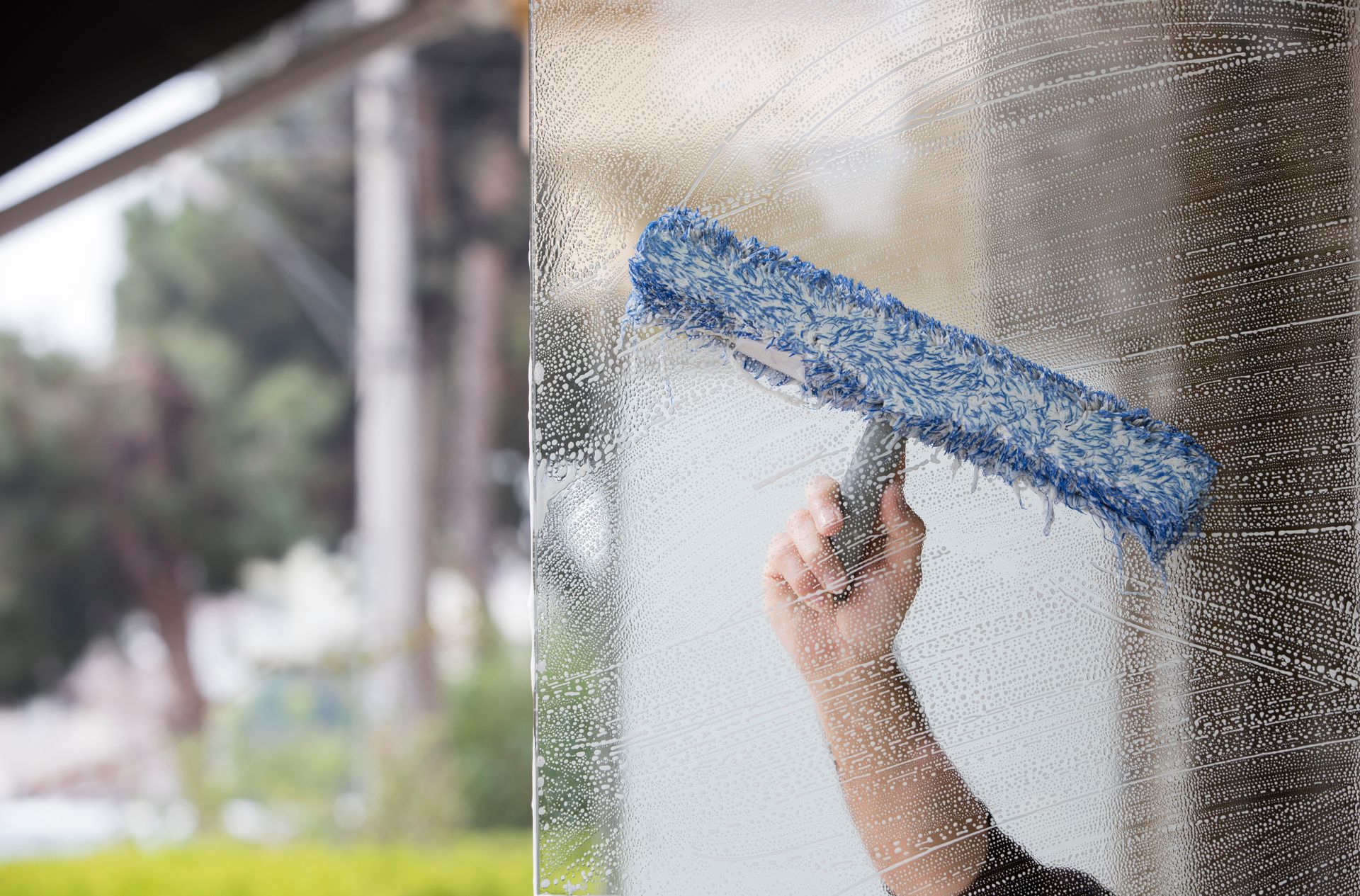 Person cleaning a window with a blue squeegee, outside setting.