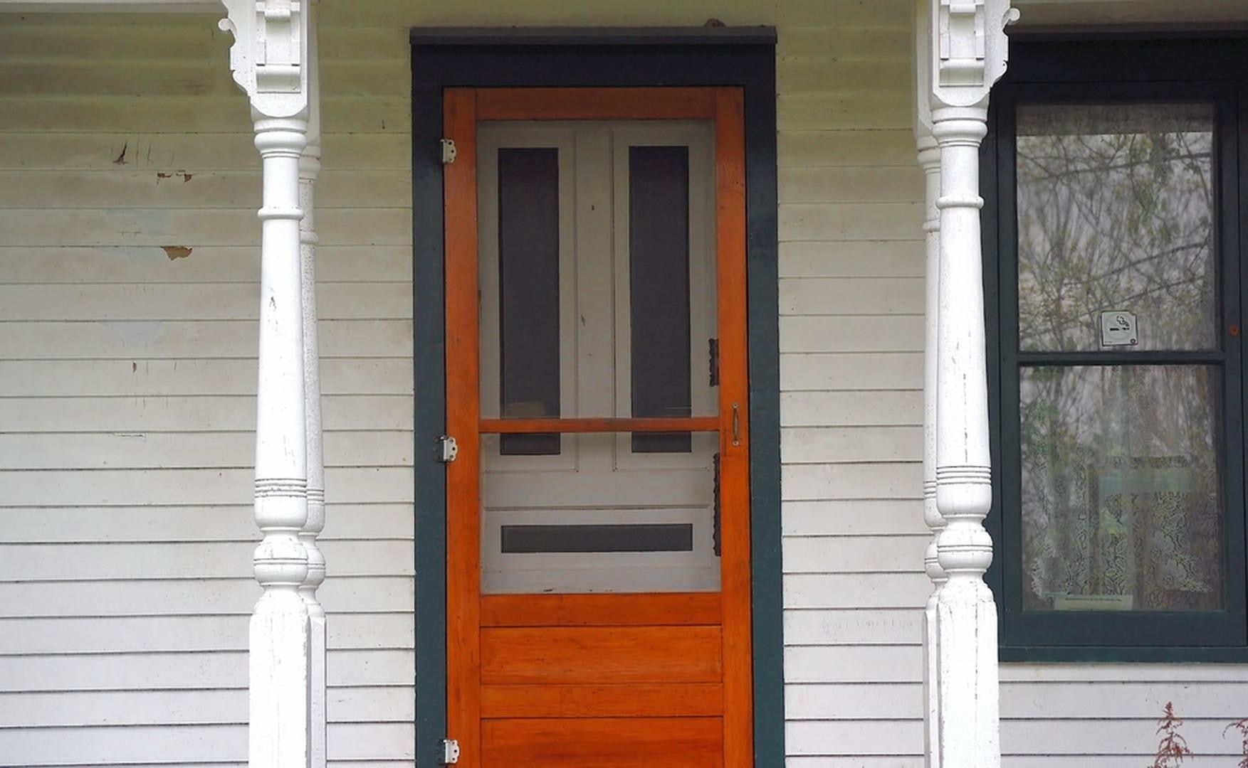 A wood-framed screen door with orange and white trim on a porch with white columns.