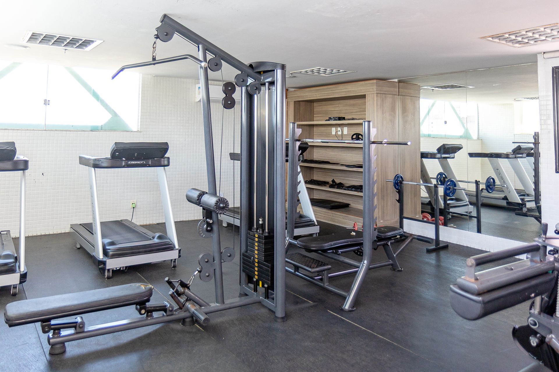 Academia com passadeiras, aparelhos de musculação e espelhos numa sala de exercícios bem iluminada