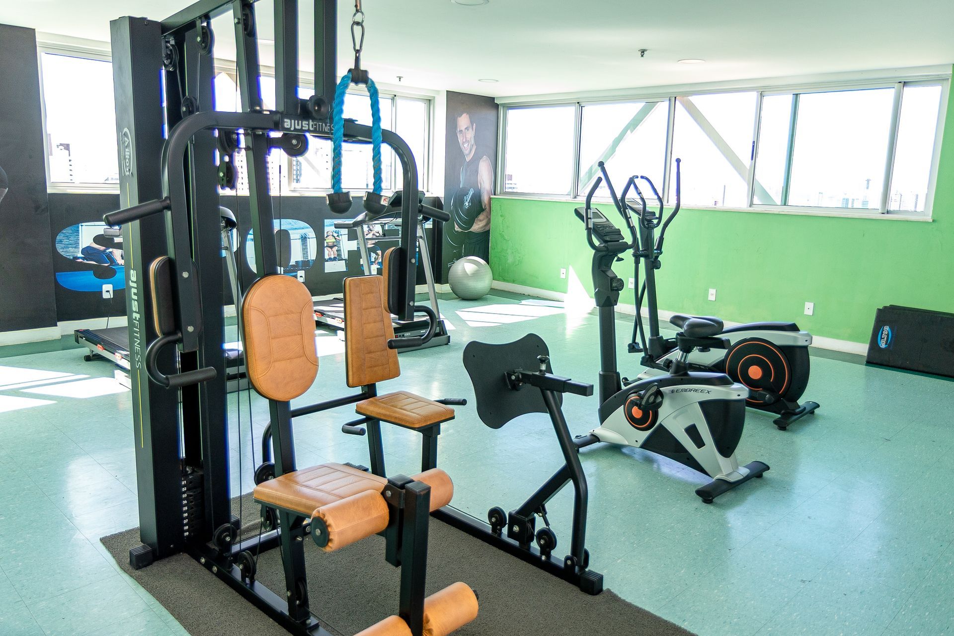 Academia moderna com aparelhos de musculação, bicicleta ergométrica, piso verde e grandes janelas.