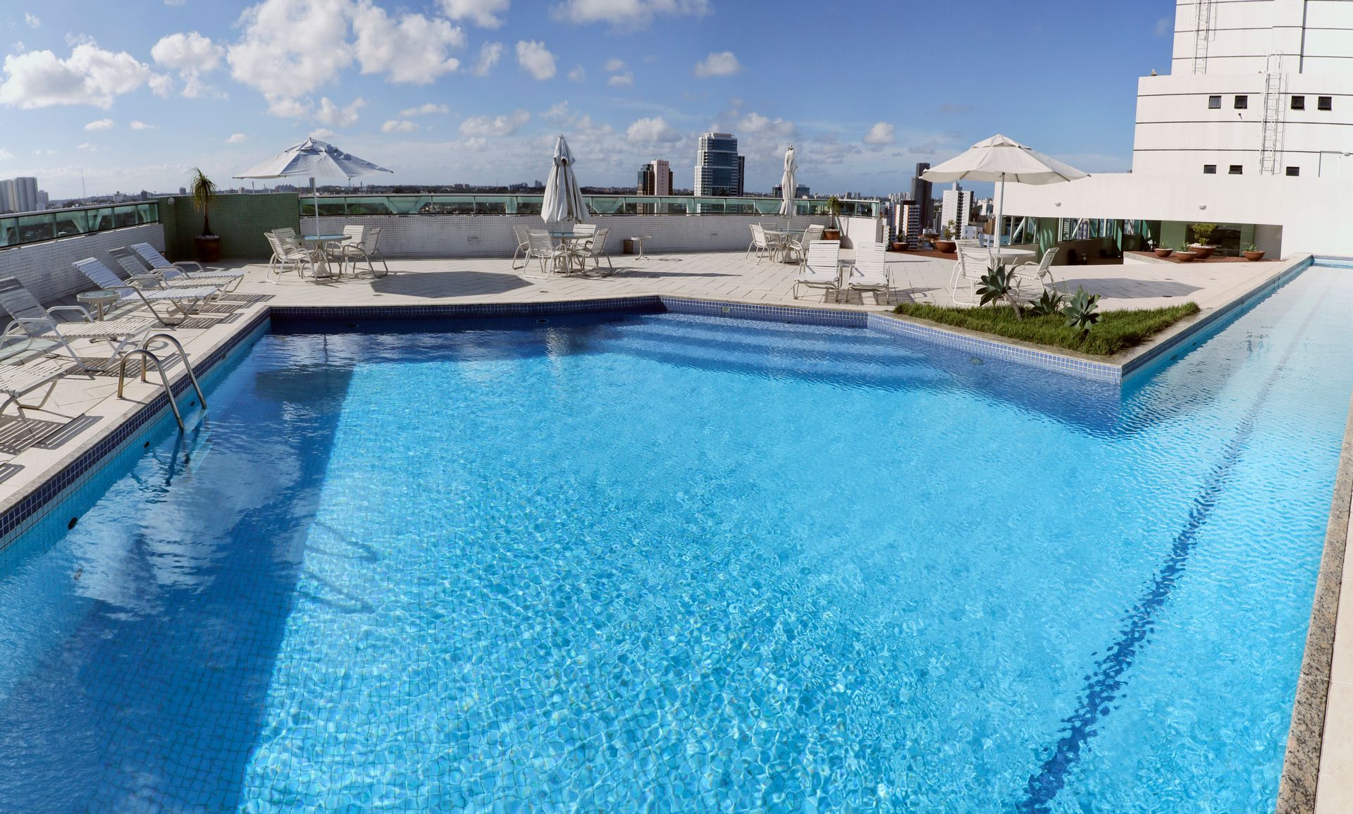 Piscina no terraço com água azul-viva, espreguiçadeiras e vista do horizonte da cidade sob um céu parcialmente nublado