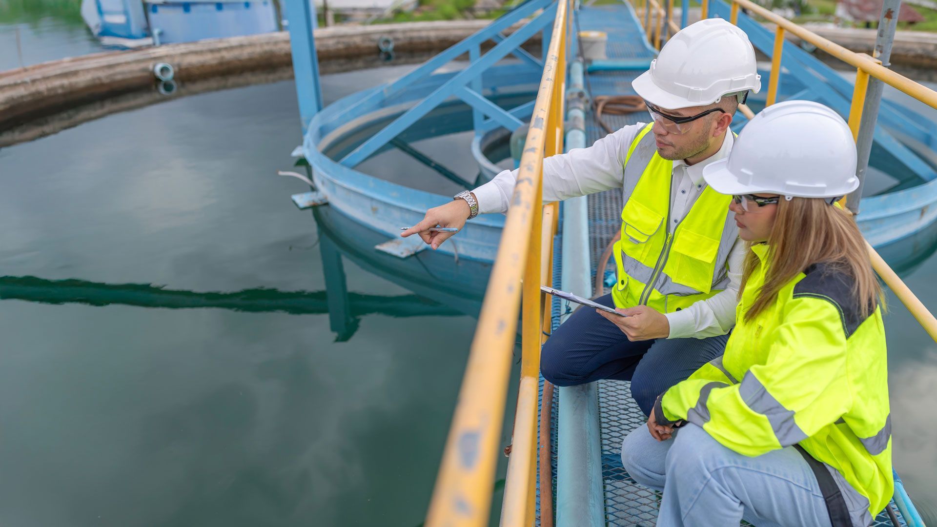Two engineers in hard hats inspect a water treatment tank beside a blue mixing mechanism