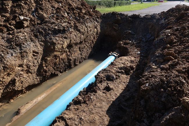 Blue pipe laid in a muddy trench beside excavated soil, leading into a small opening