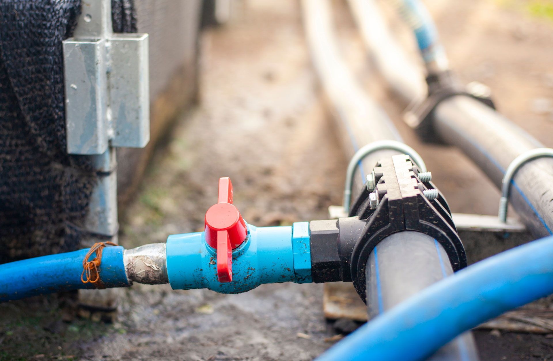 Blue pipe with red valve and black clamp on a dirt construction site
