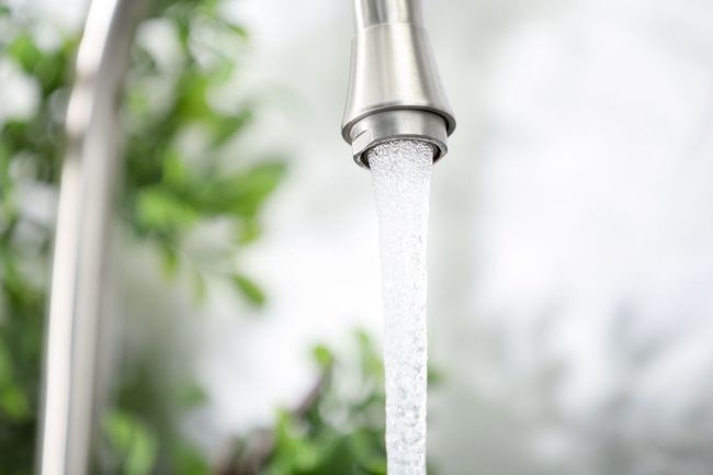 Close-up of water flowing from a metal faucet into a sink, with a blurred green background