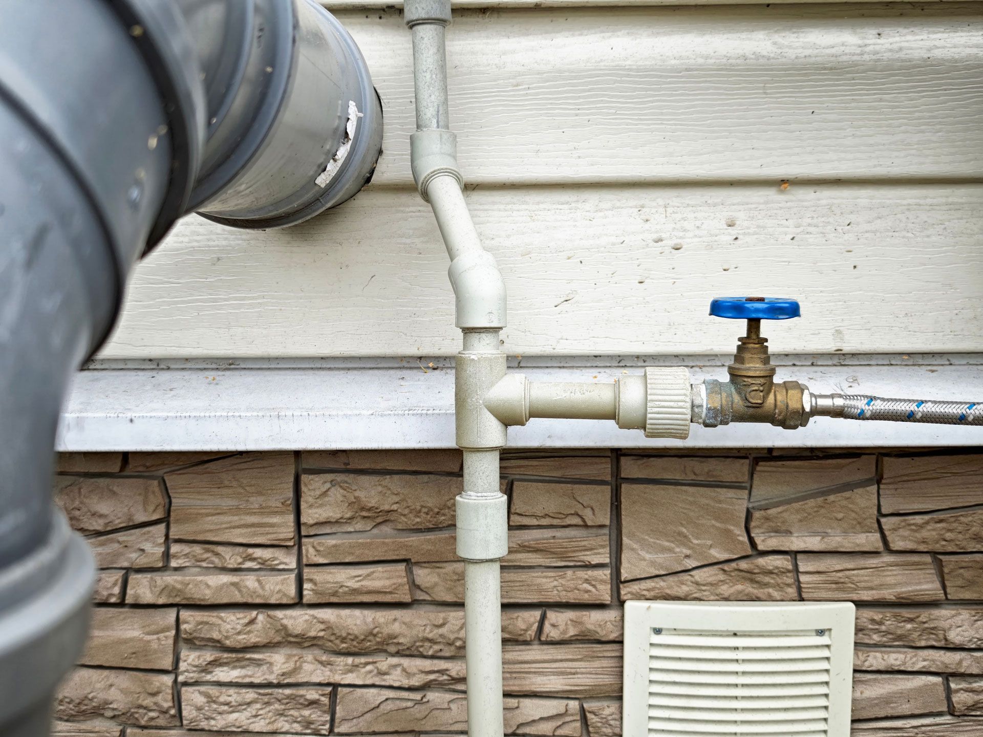 Outdoor utility pipes and a blue-handled valve mounted on a house exterior wall