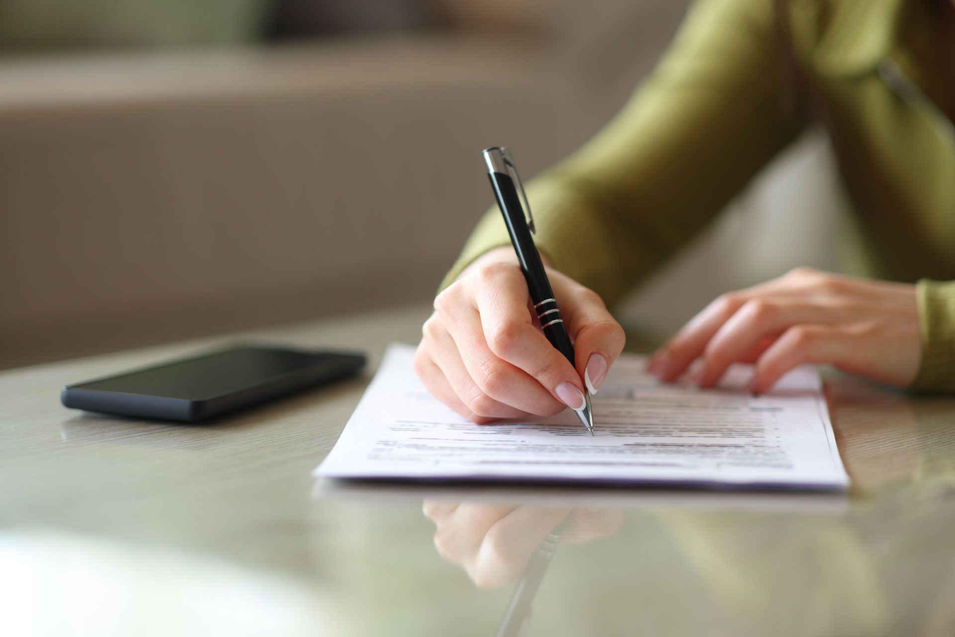 Hand writing on a notebook at a desk beside a smartphone