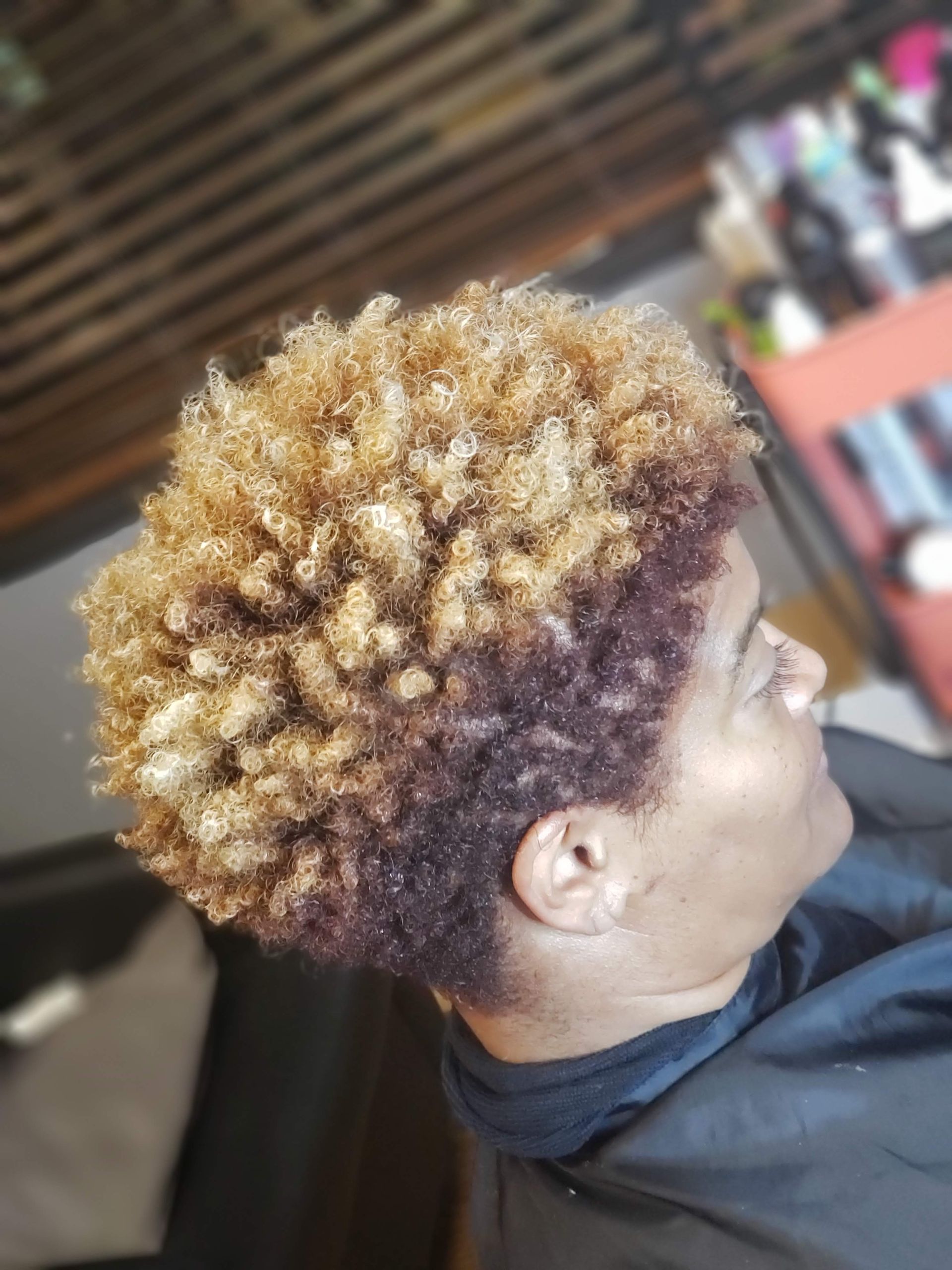 Woman with short, textured hair dyed blonde on top and deep red underneath, at a salon.