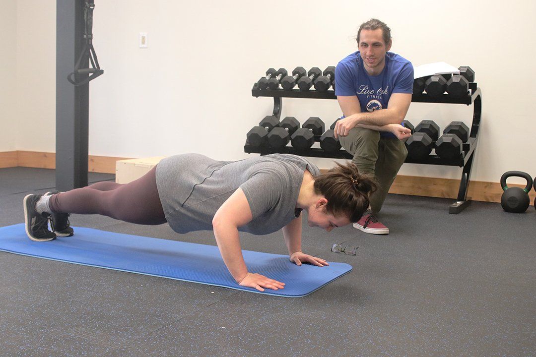 A man is watching a woman do push ups on a mat in a gym.