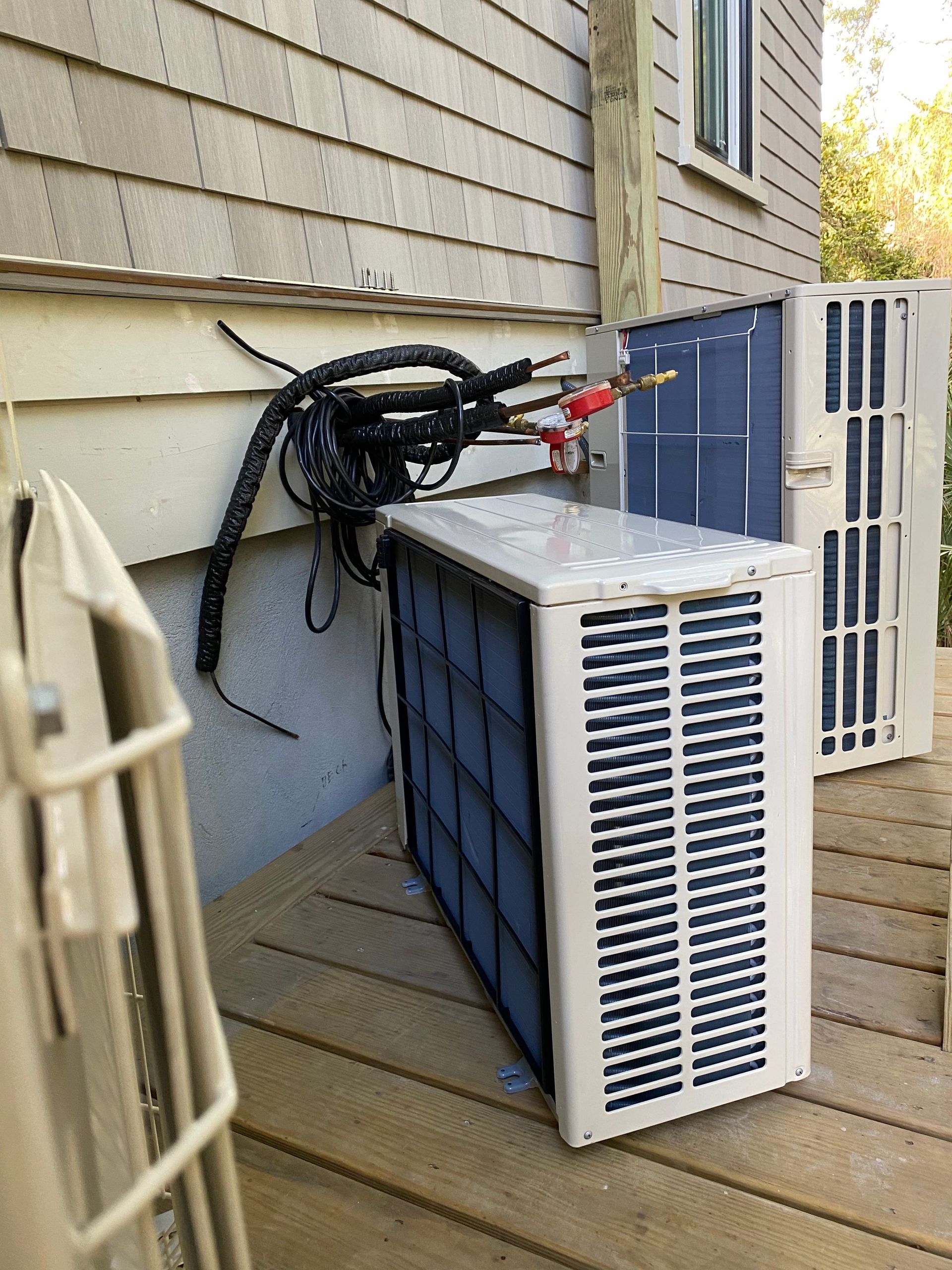A person in a protective suit sprays a blue protective coating onto an HVAC coil outdoors.