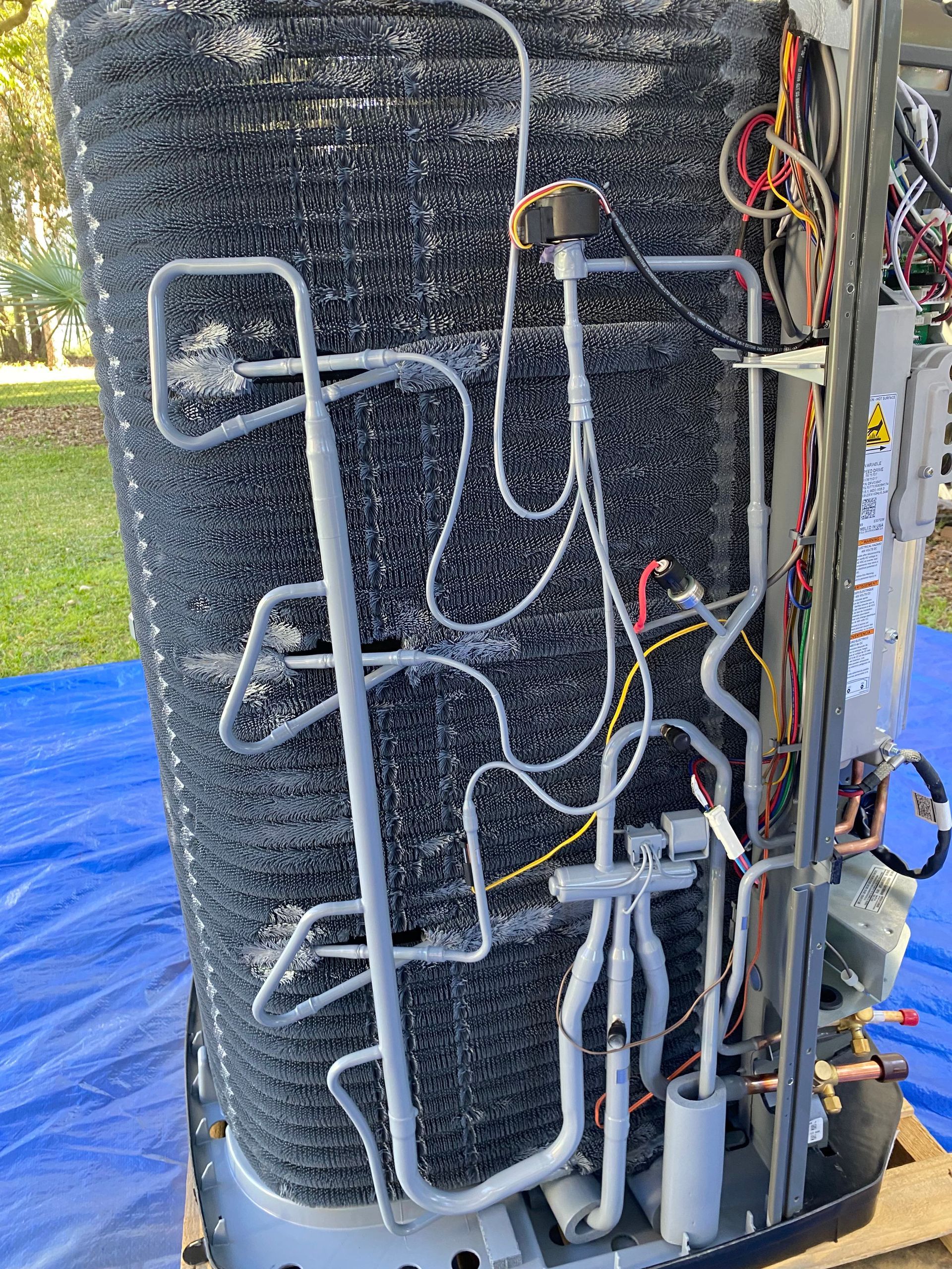 An open HVAC unit cabinet showing two grey vertical compressors connected by pipes and wiring against a metal frame.