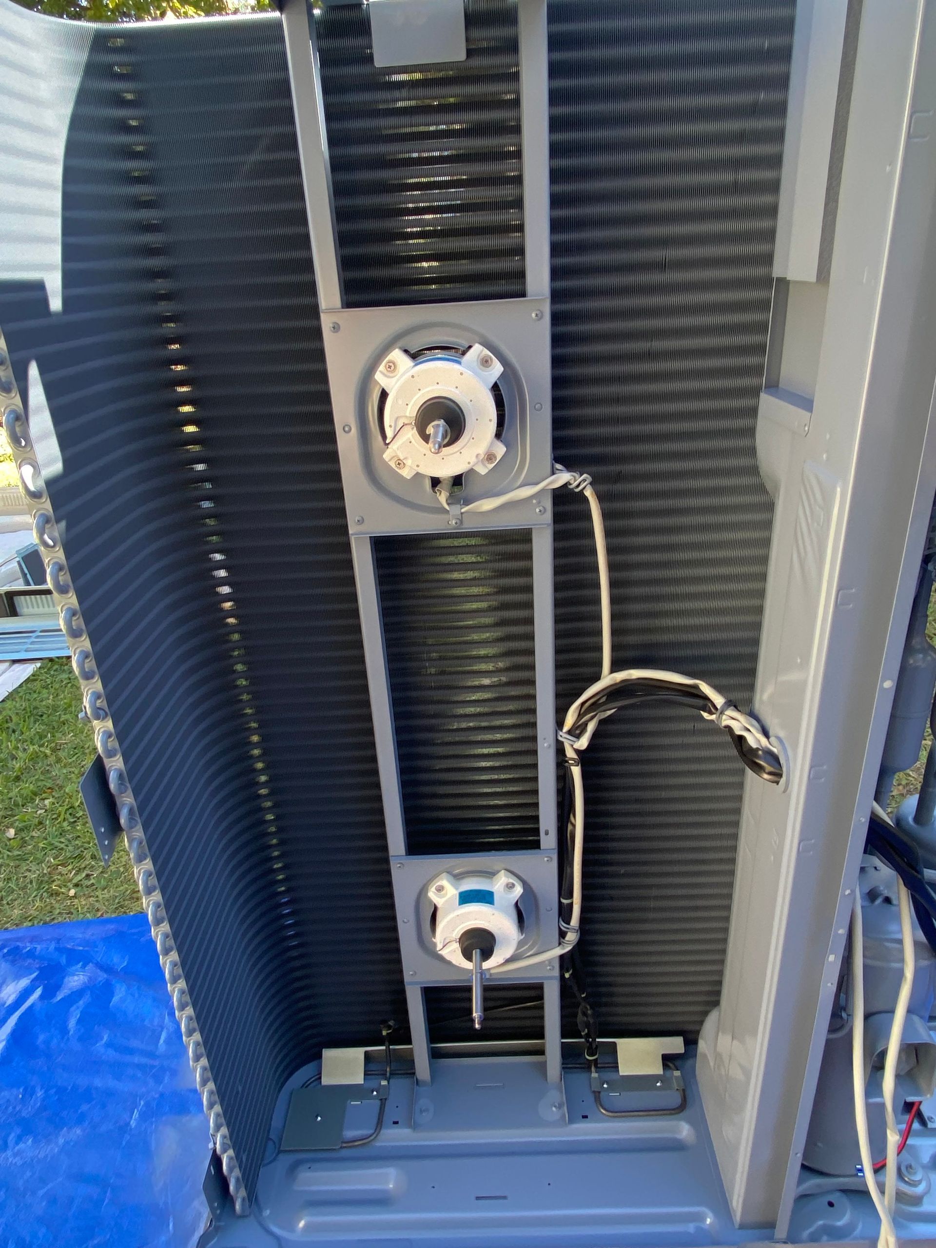 A person in a protective suit sprays a blue protective coating onto an HVAC coil outdoors.