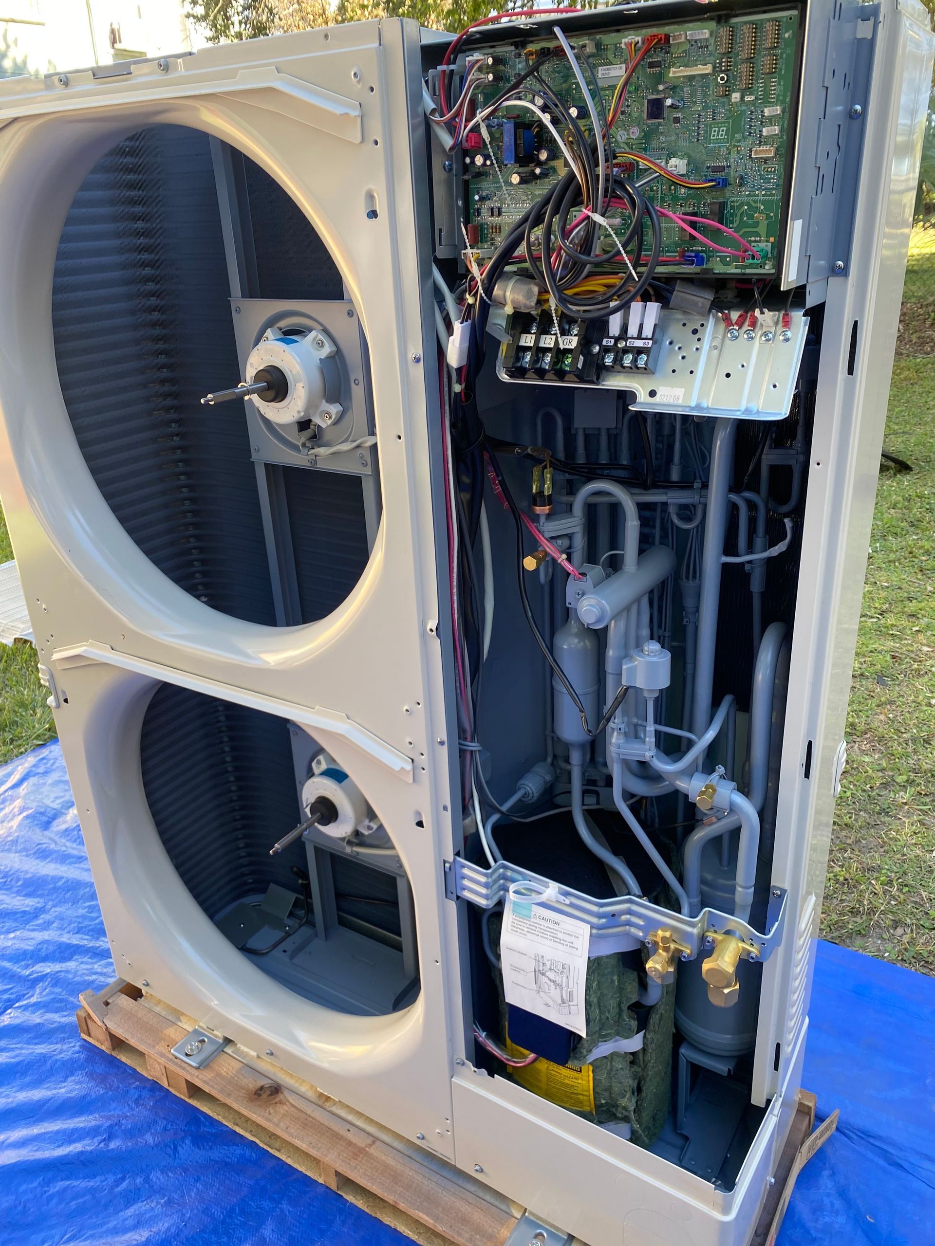 The internal components of an industrial HVAC unit are shown, featuring wiring, circuit boards, and a grey compressor.