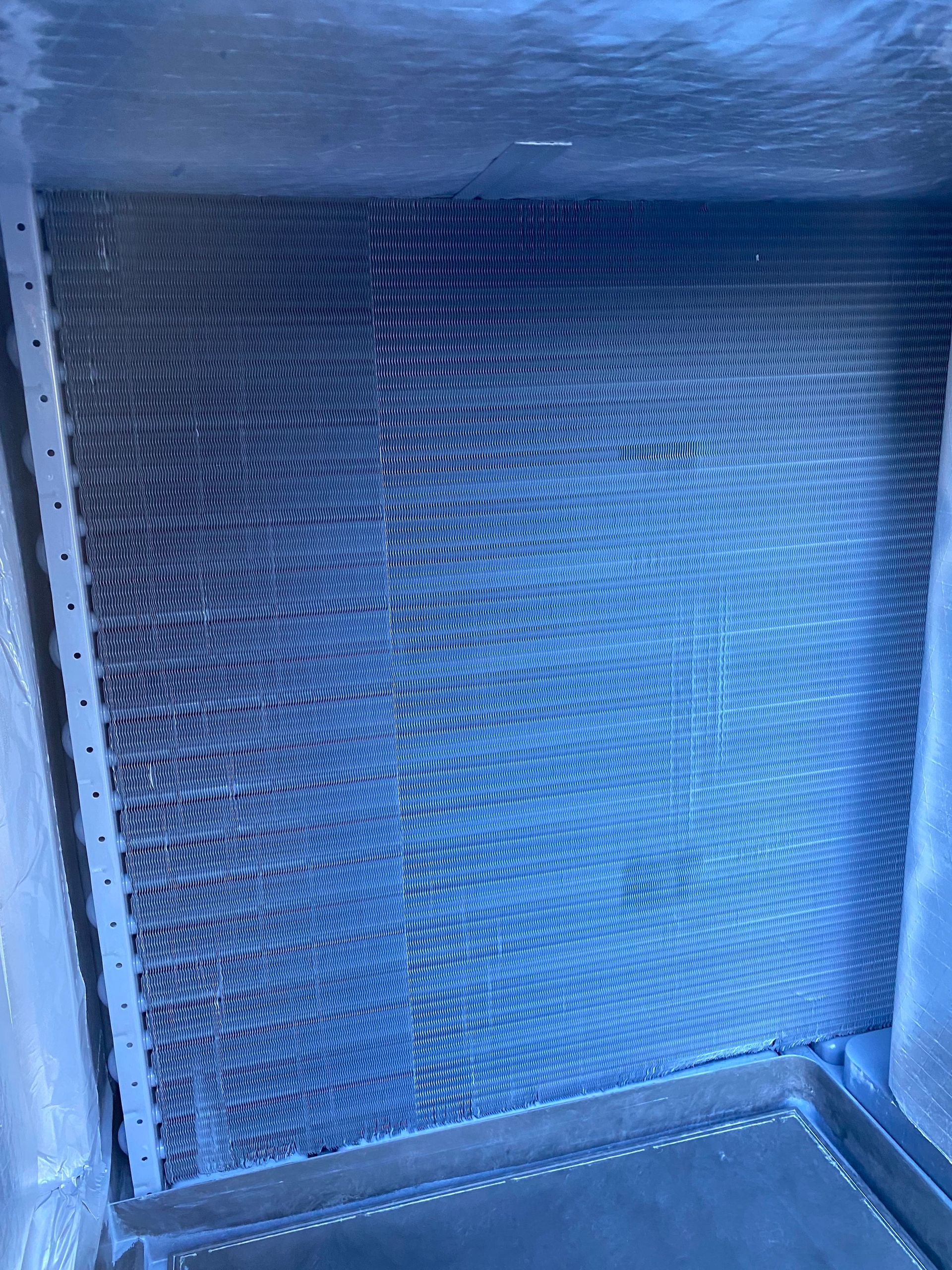 A blue air conditioner condenser coil and internal copper piping mounted on a wooden pallet.