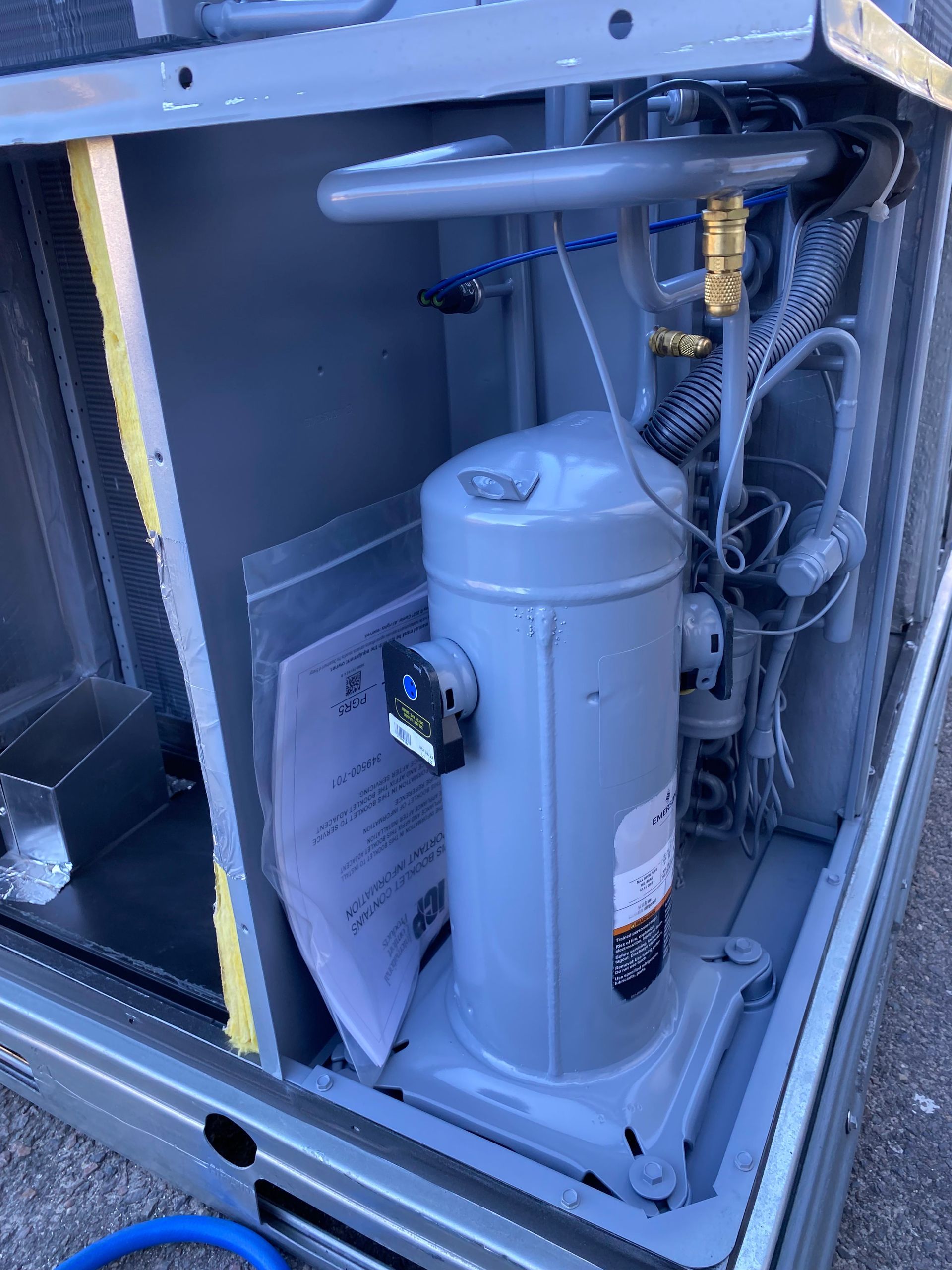 A person in a protective suit sprays a blue protective coating onto an HVAC coil outdoors.