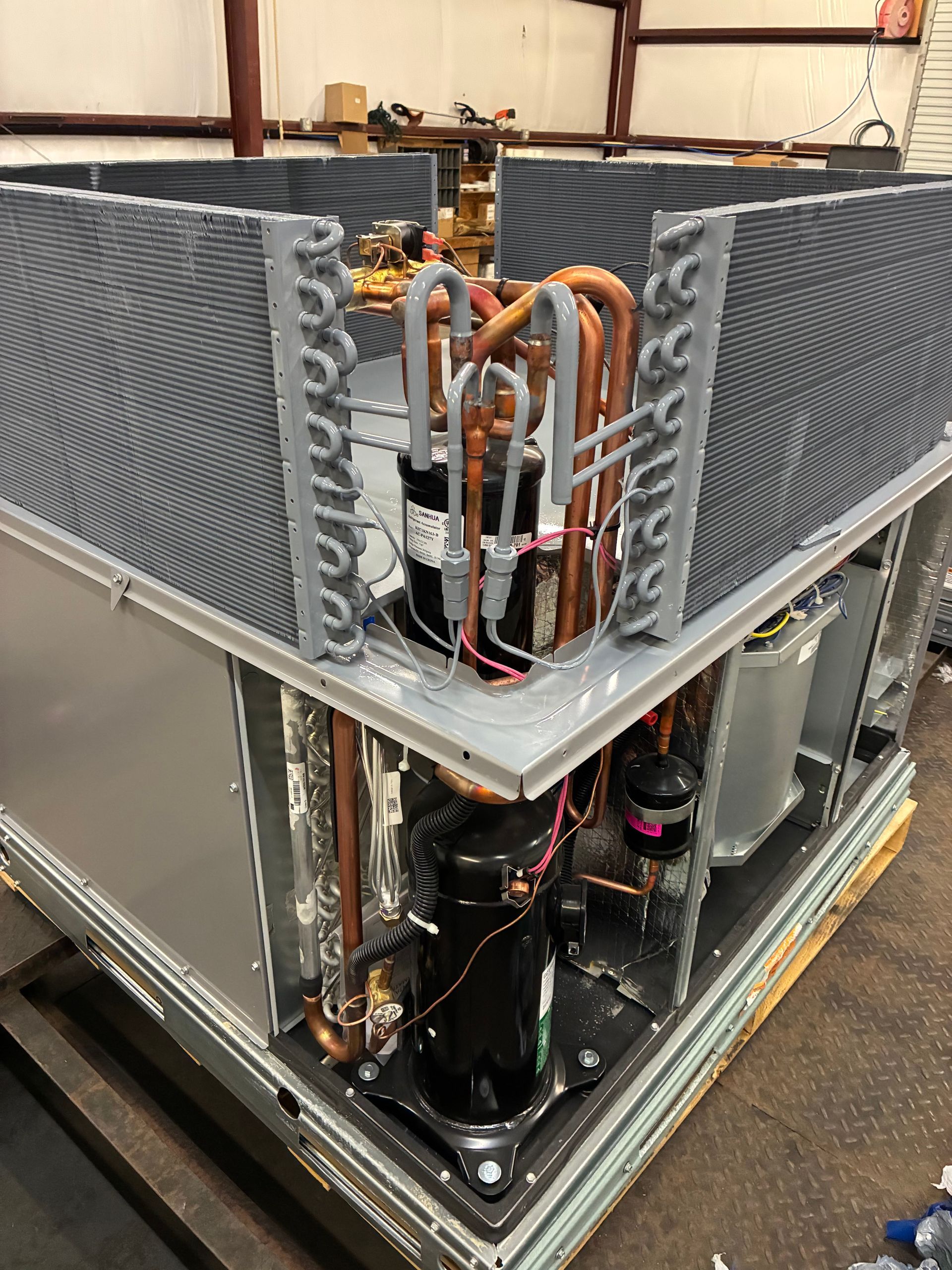 The interior of an HVAC air handler unit featuring an A-frame evaporator coil assembly with metal tubing and drain ports.