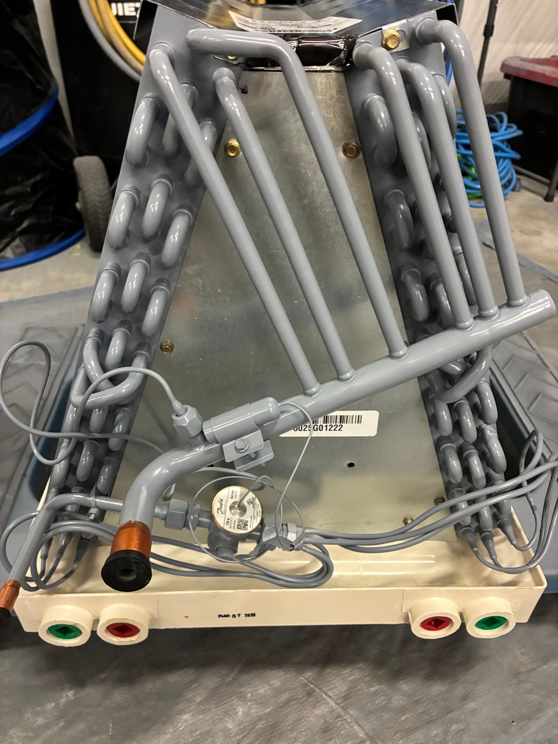 A dirty air conditioner evaporator coil sits beside a clean replacement coil on a tiled floor in a room.