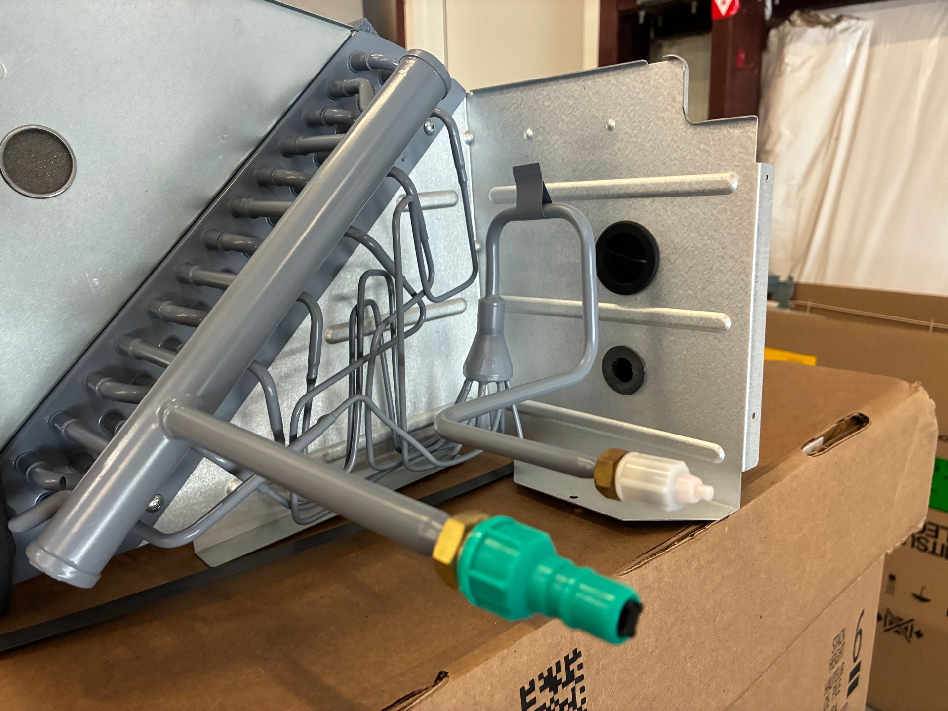 A person in a blue glove uses a spray nozzle to clean a blue industrial heat exchanger coil in a factory.
