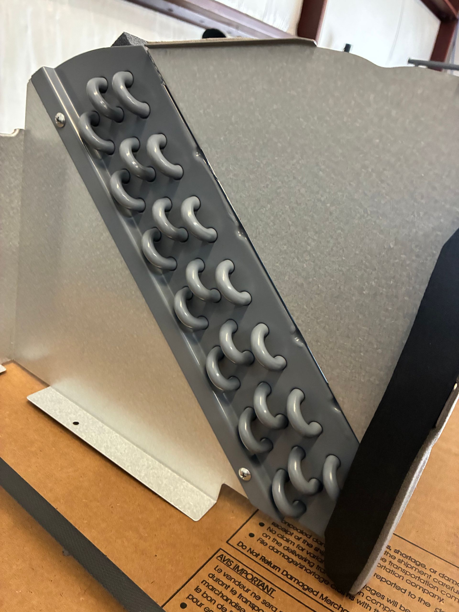 The interior of an HVAC air handler unit featuring an A-frame evaporator coil assembly with metal tubing and drain ports.