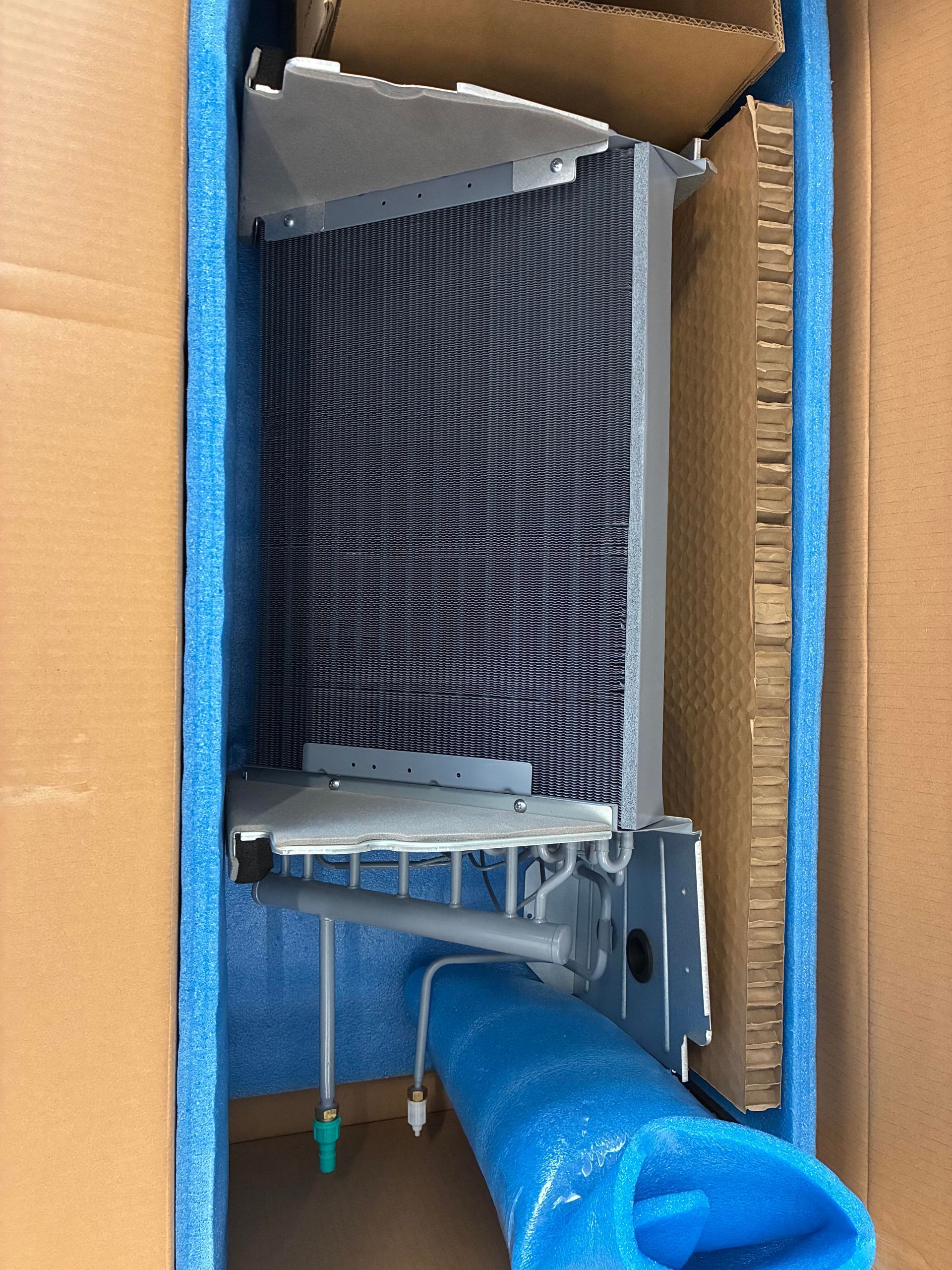 A person in a protective suit sprays a blue protective coating onto an HVAC coil outdoors.