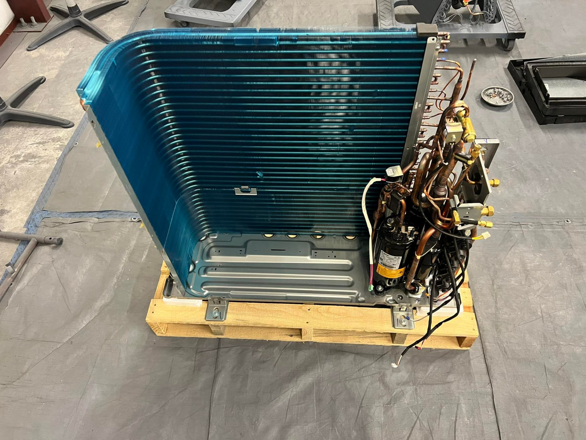 A blue air conditioner condenser coil and internal copper piping mounted on a wooden pallet.