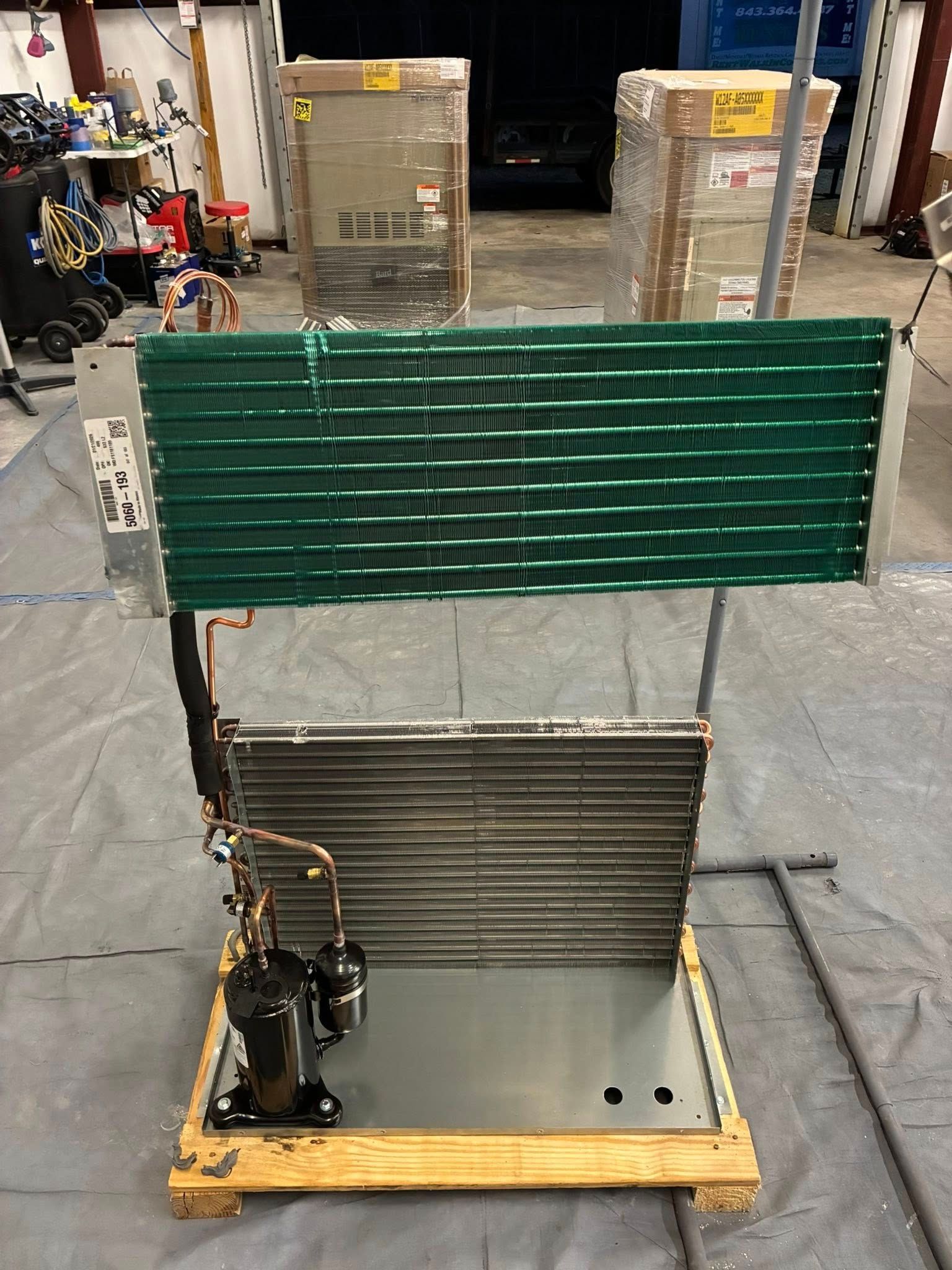 A refrigeration cooling unit with a green coil, a gray condenser coil, and a black compressor on a wooden pallet base.