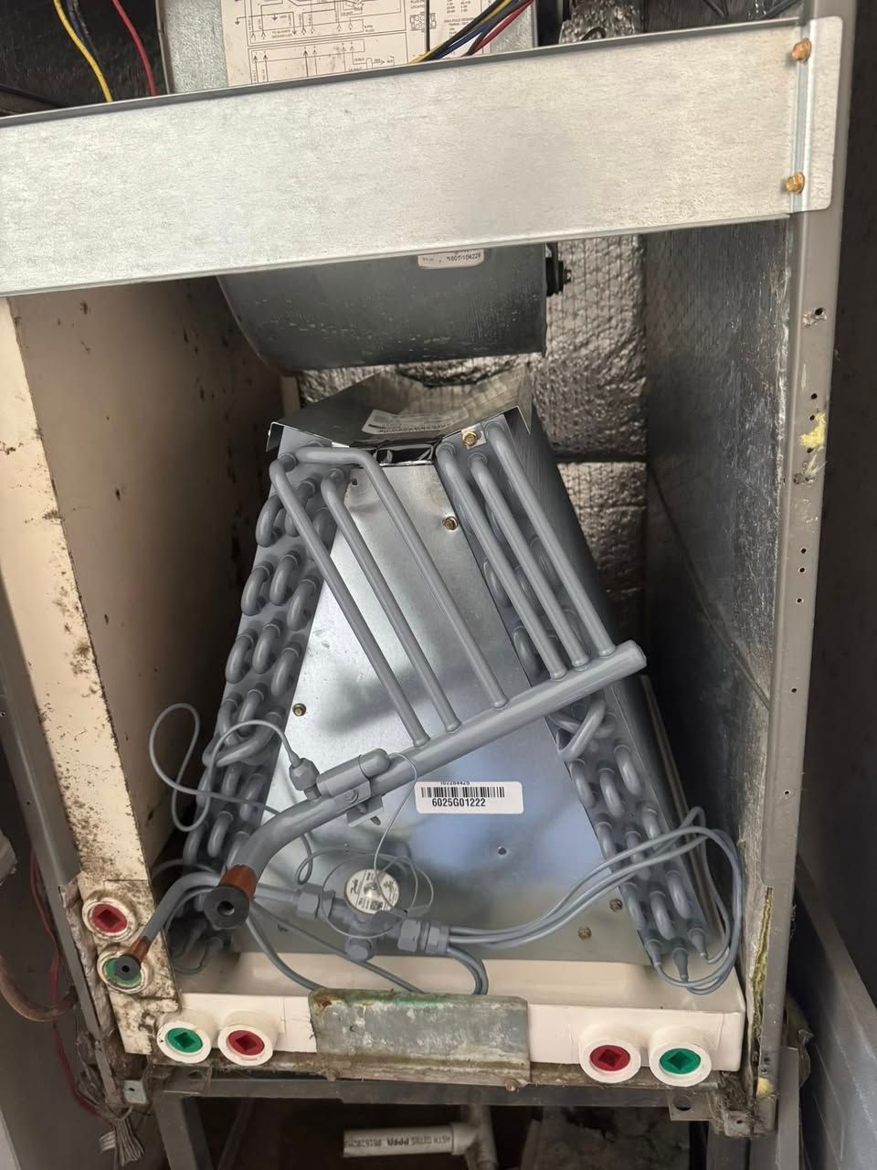 The interior of an HVAC air handler unit featuring an A-frame evaporator coil assembly with metal tubing and drain ports.