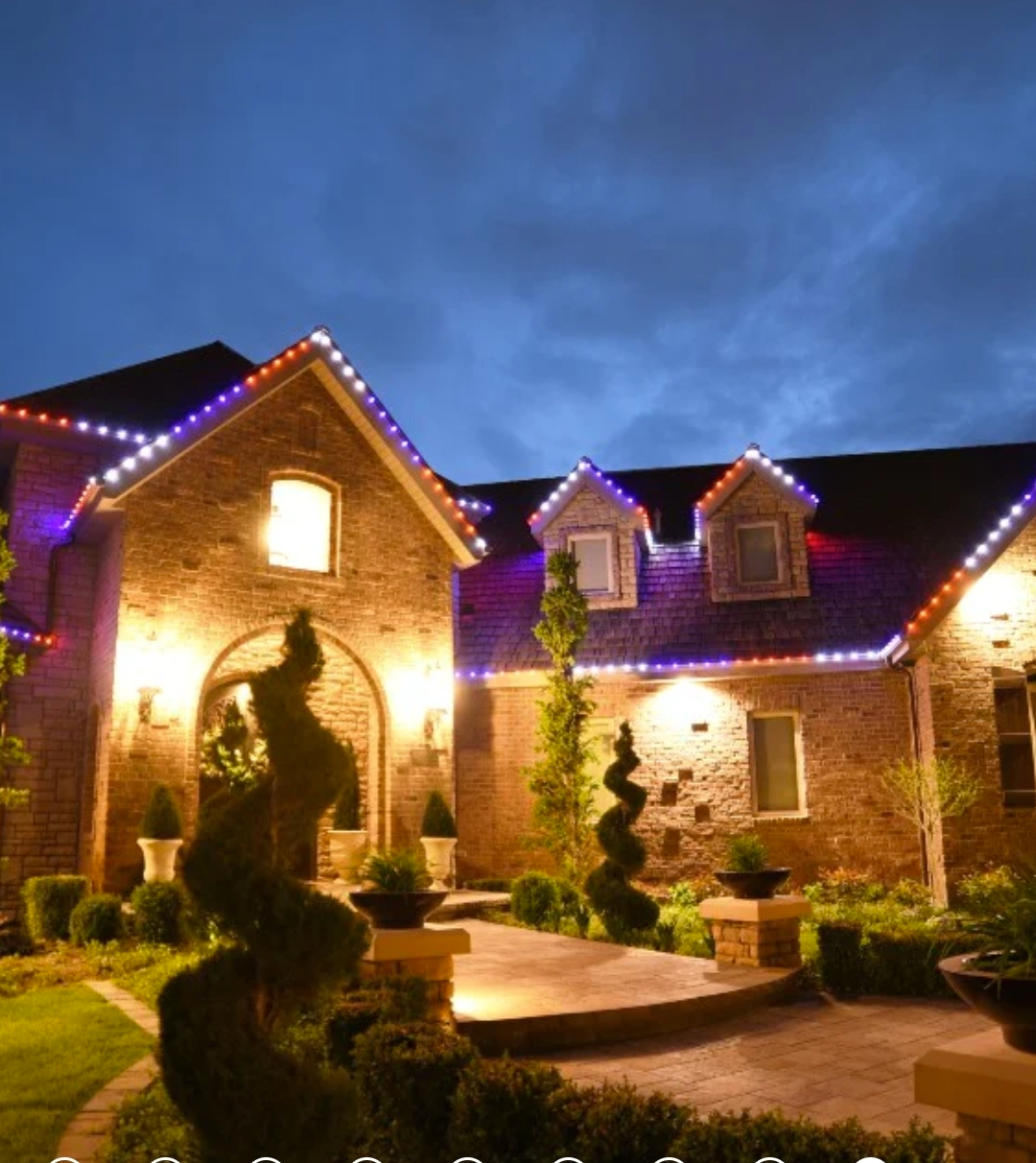 Brick house with red and blue Christmas lights on the roof, lit walkway at night.