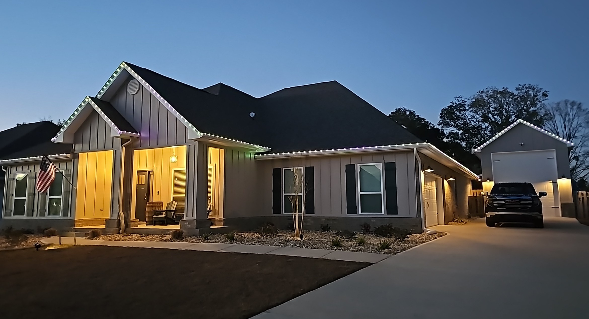 Front view of a gray house with a black door, white garage, and brown lawn.