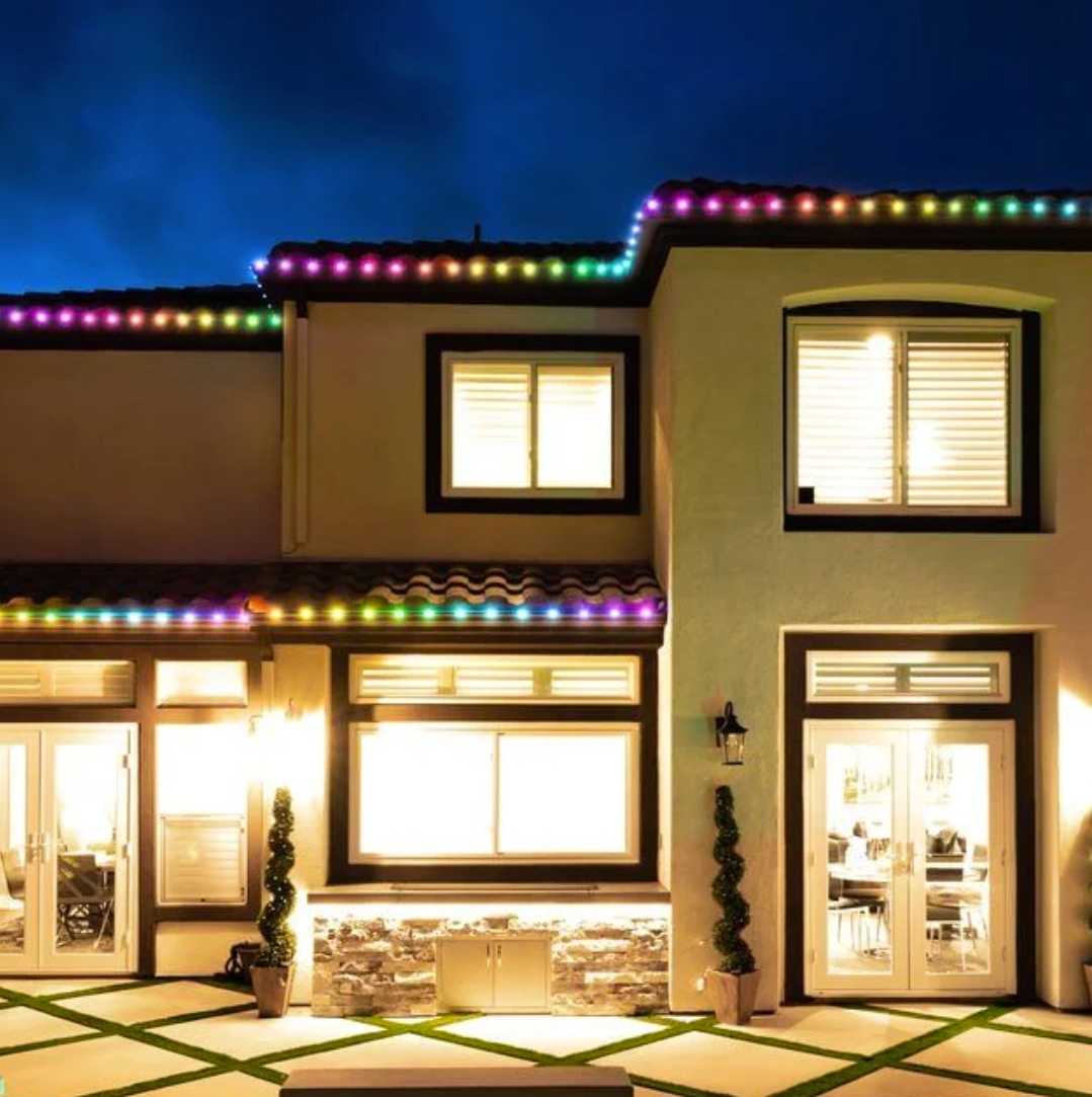 House at night with colorful lights along the roofline and palm trees under a starry sky.